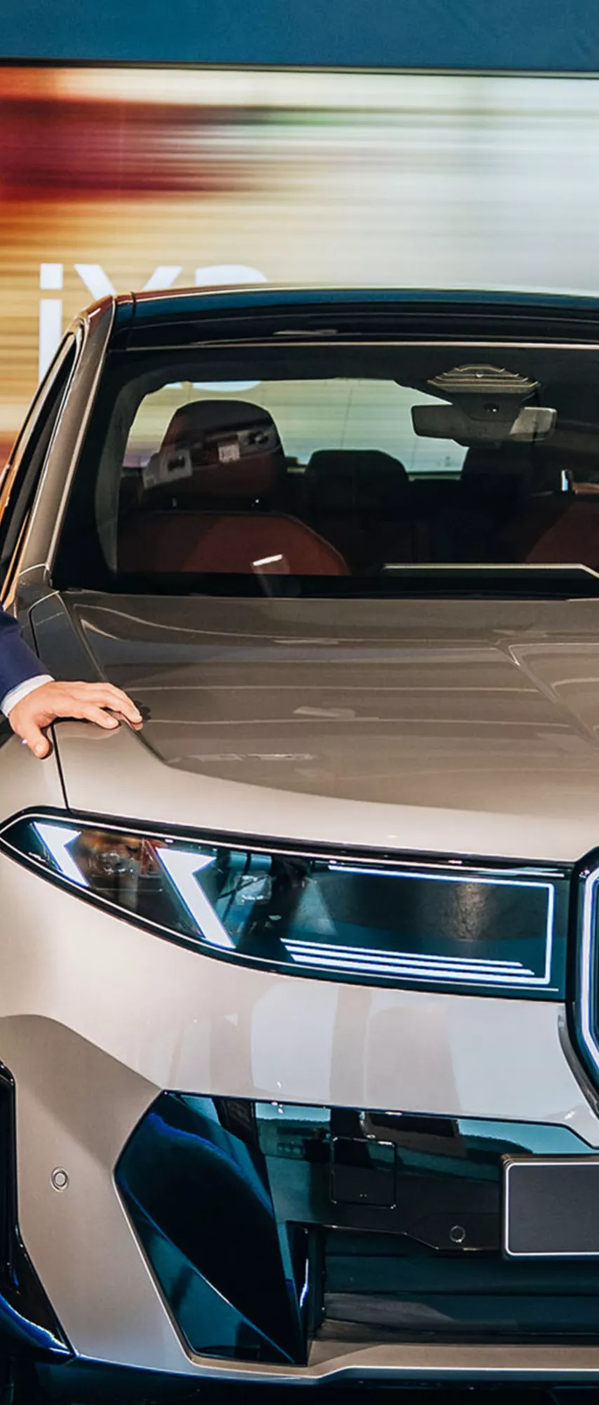 Sindre Sandberg står ved siden av en beige BMW iX3 sett forfra