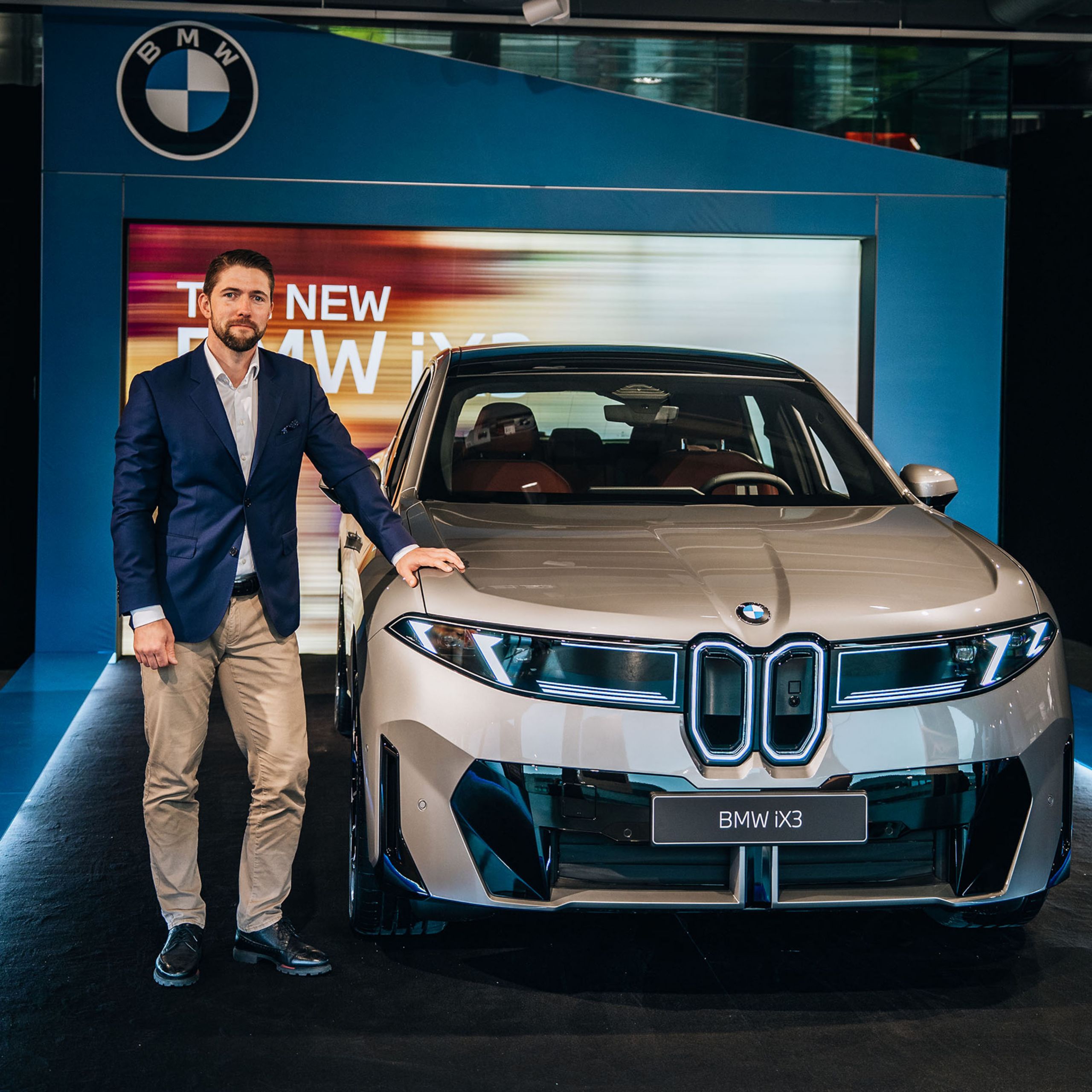 Sindre Sandberg står ved siden av en beige BMW iX3 sett forfra