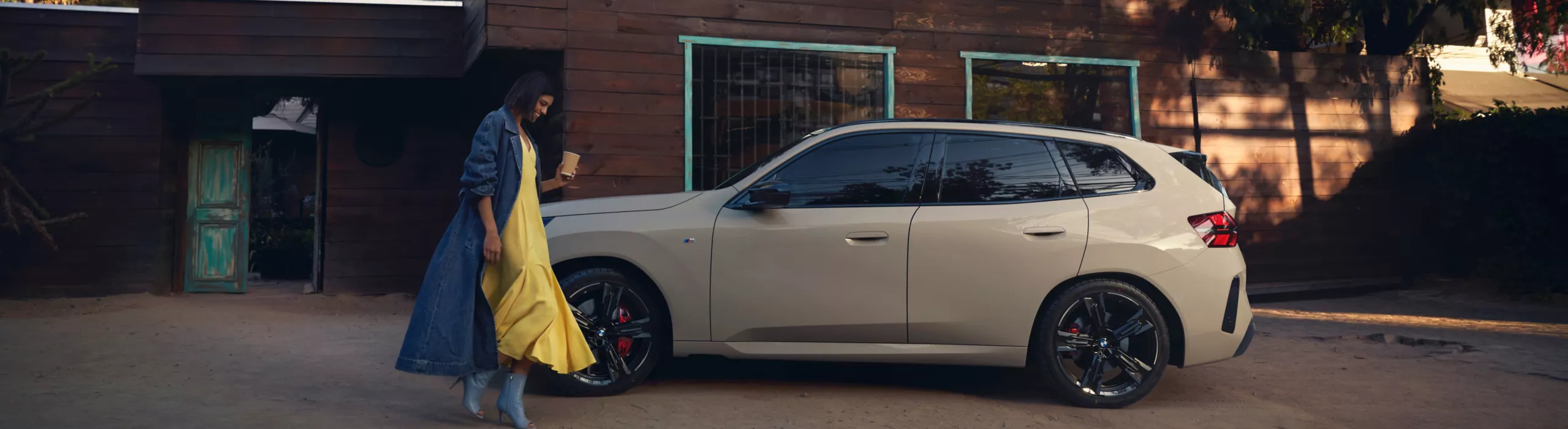 Man leans on his BMW with a surfboard on the roof rack. Another surfboard leans on the vehicle with a river and bridge in the background