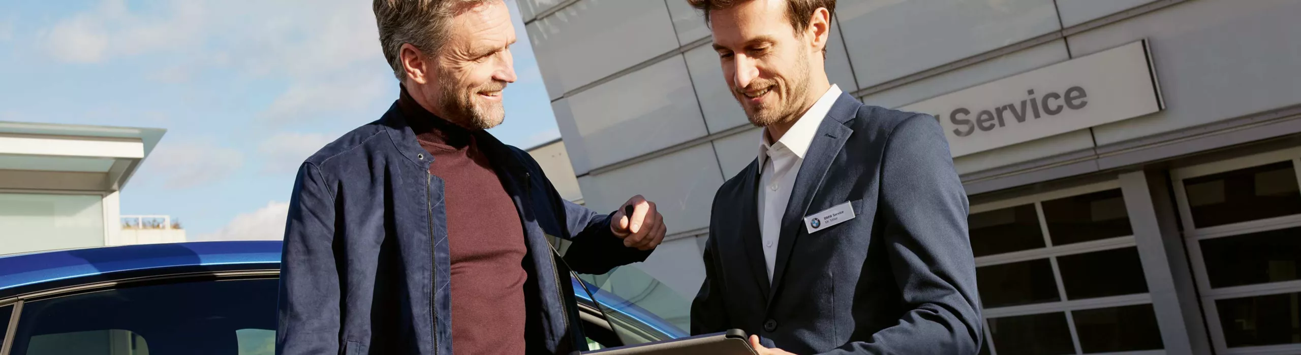 Kunde und Händler stehen mit einem Tablet vor einem BMW