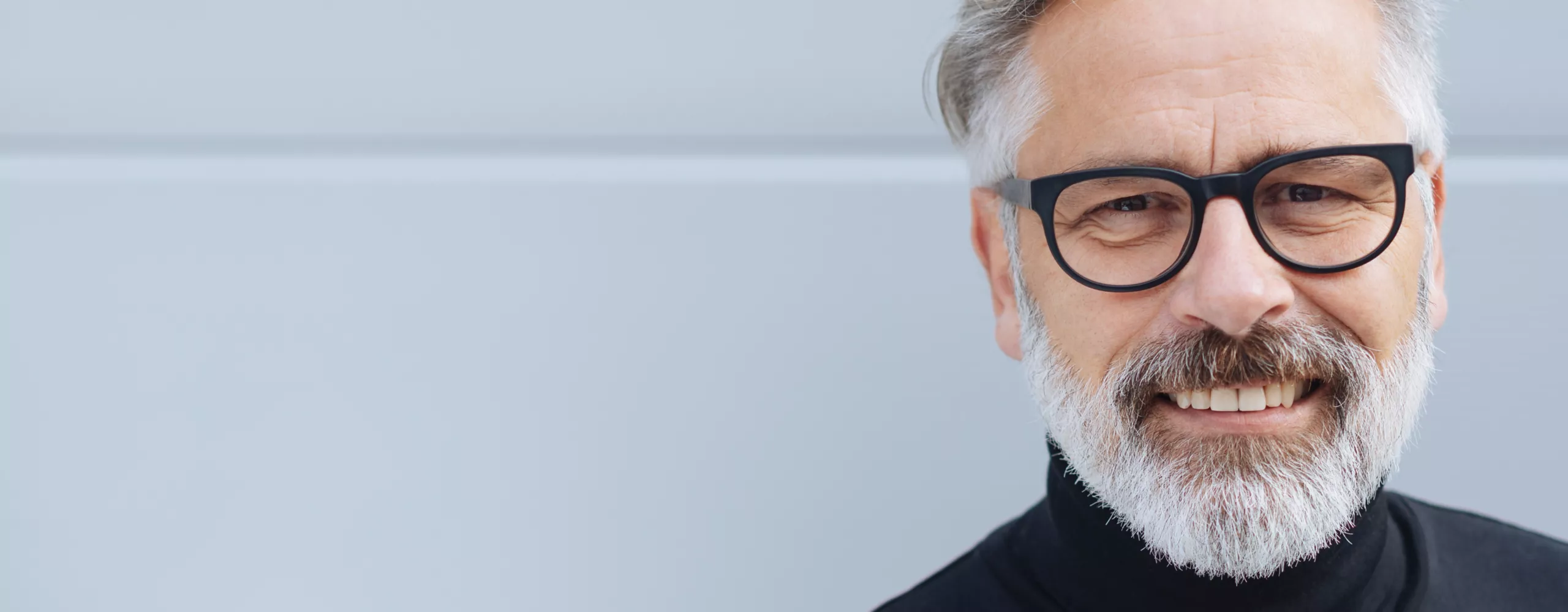 Älterer Mann mit Brille lacht in die Kamera. 