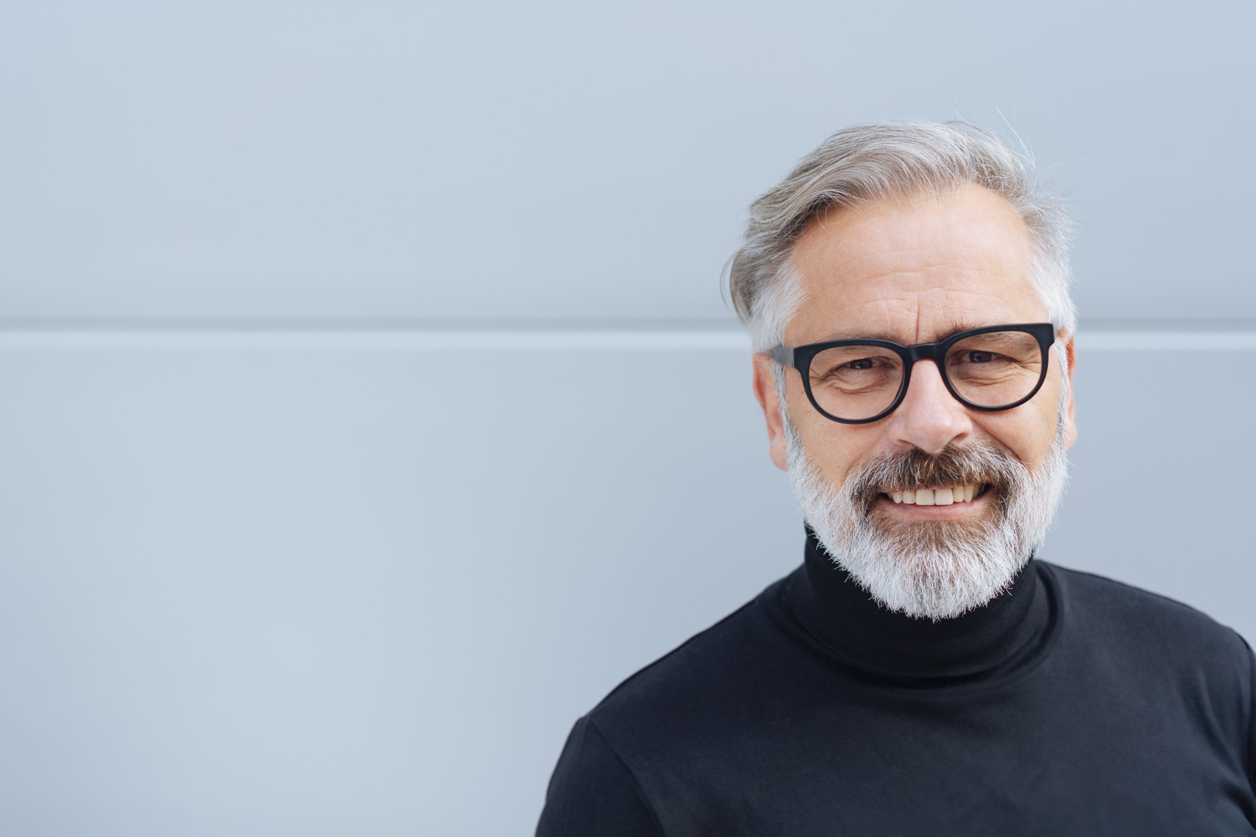 Älterer Mann mit Brille lacht in die Kamera. 