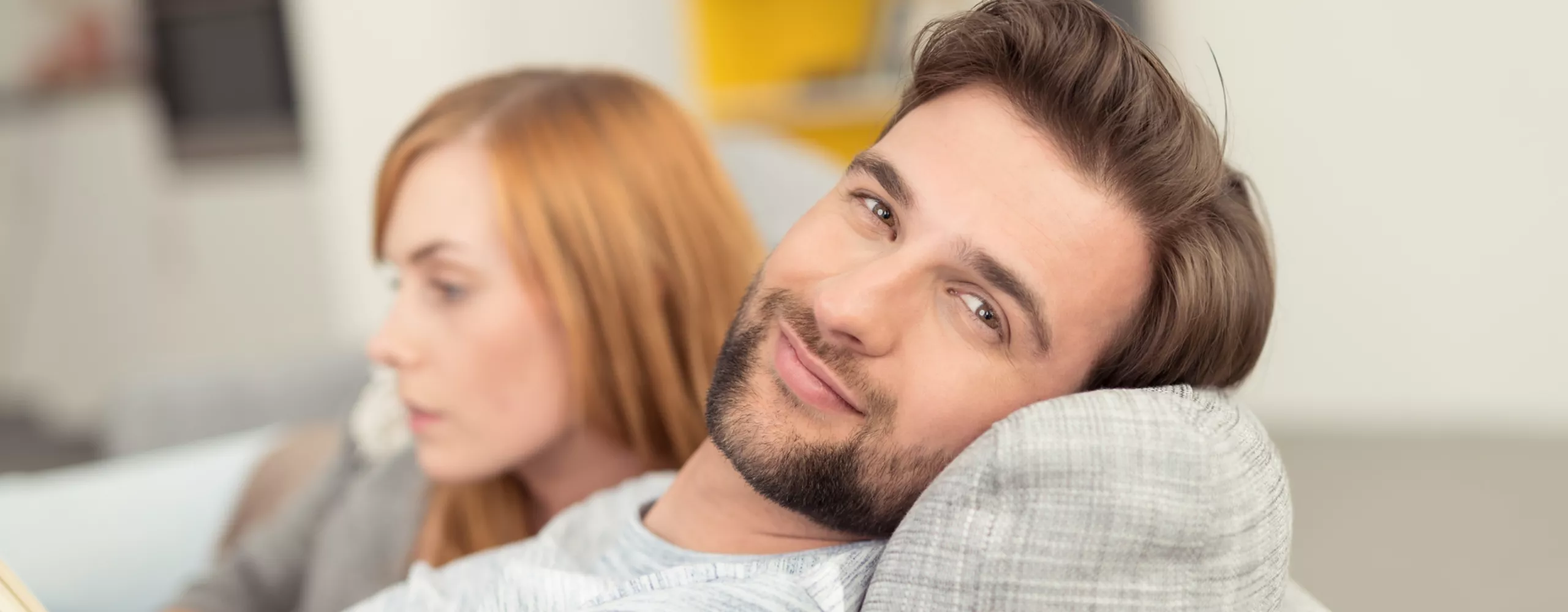 Mann und Frau liegen auf der Couch, Mann lächelt in Kamera