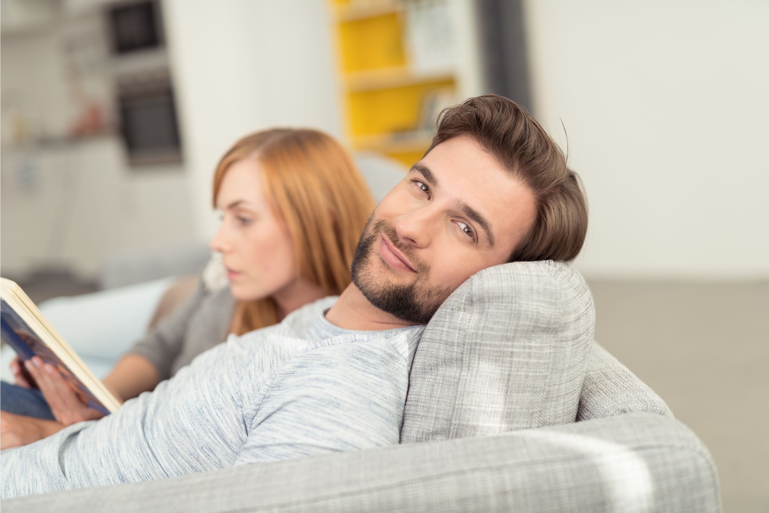Mann und Frau liegen auf der Couch, Mann lächelt in Kamera