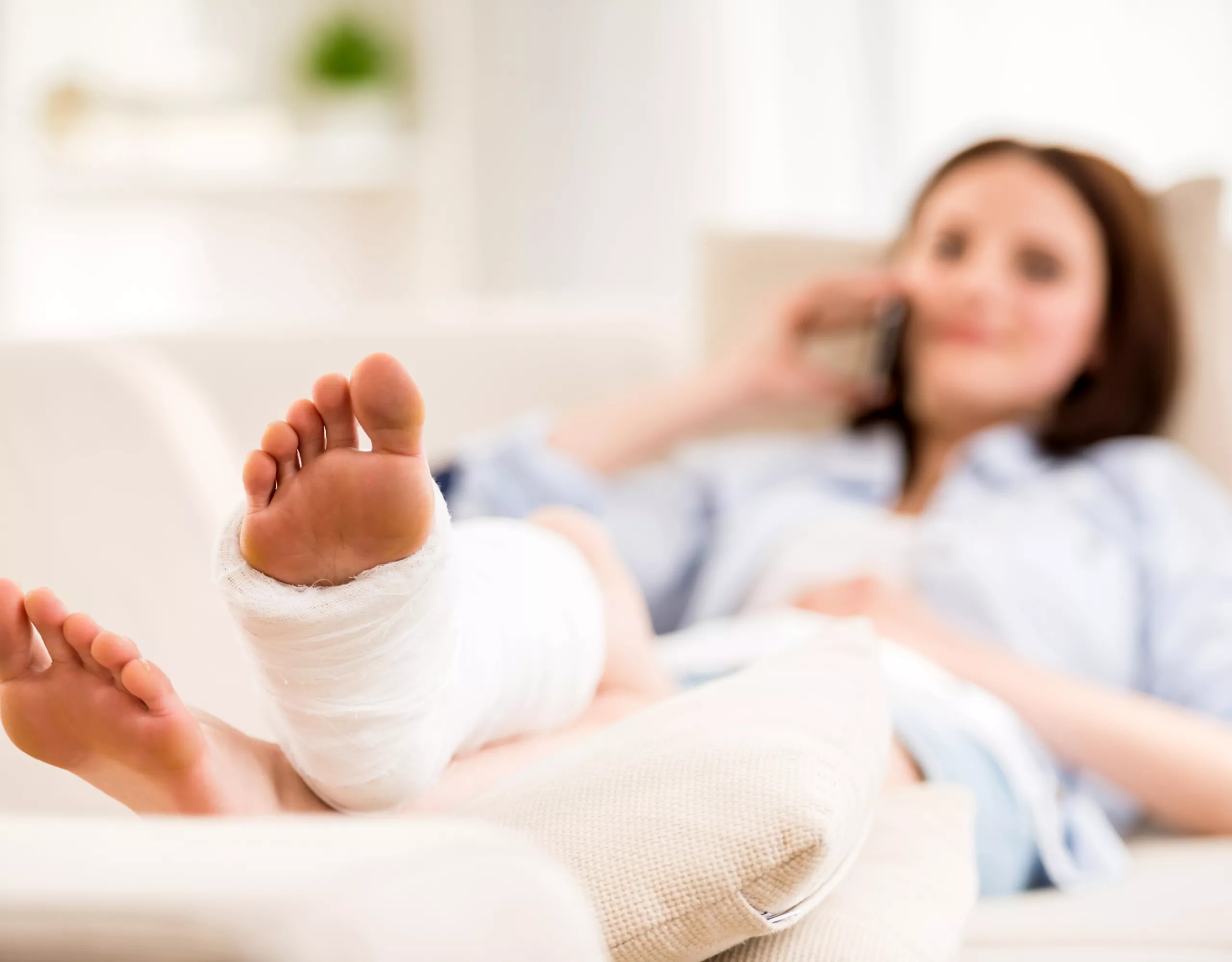 Frau liegt mit Verband am Fuß auf dem Sofa