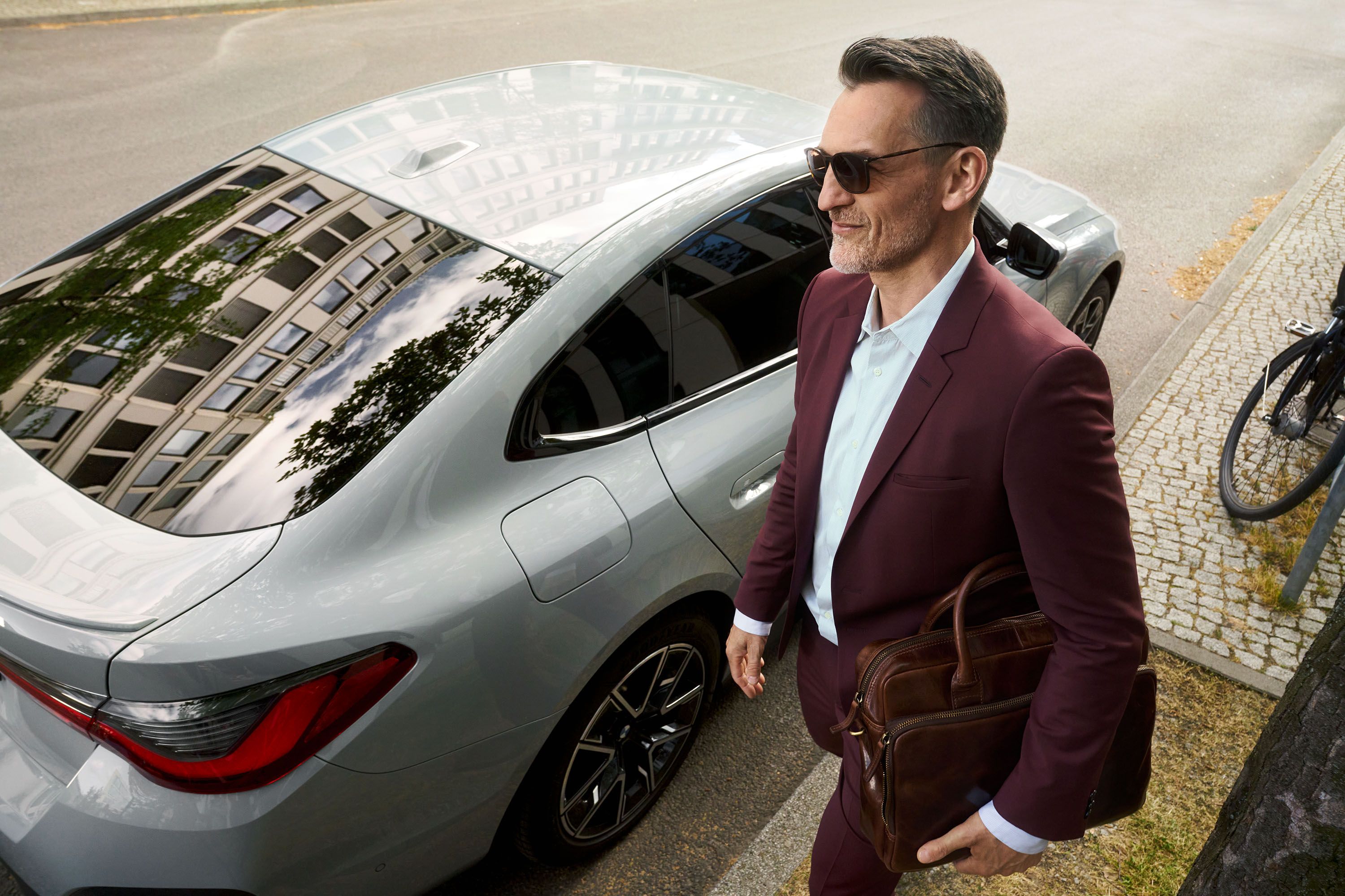 En man i kostym som går vid sidan av en grå BMW
