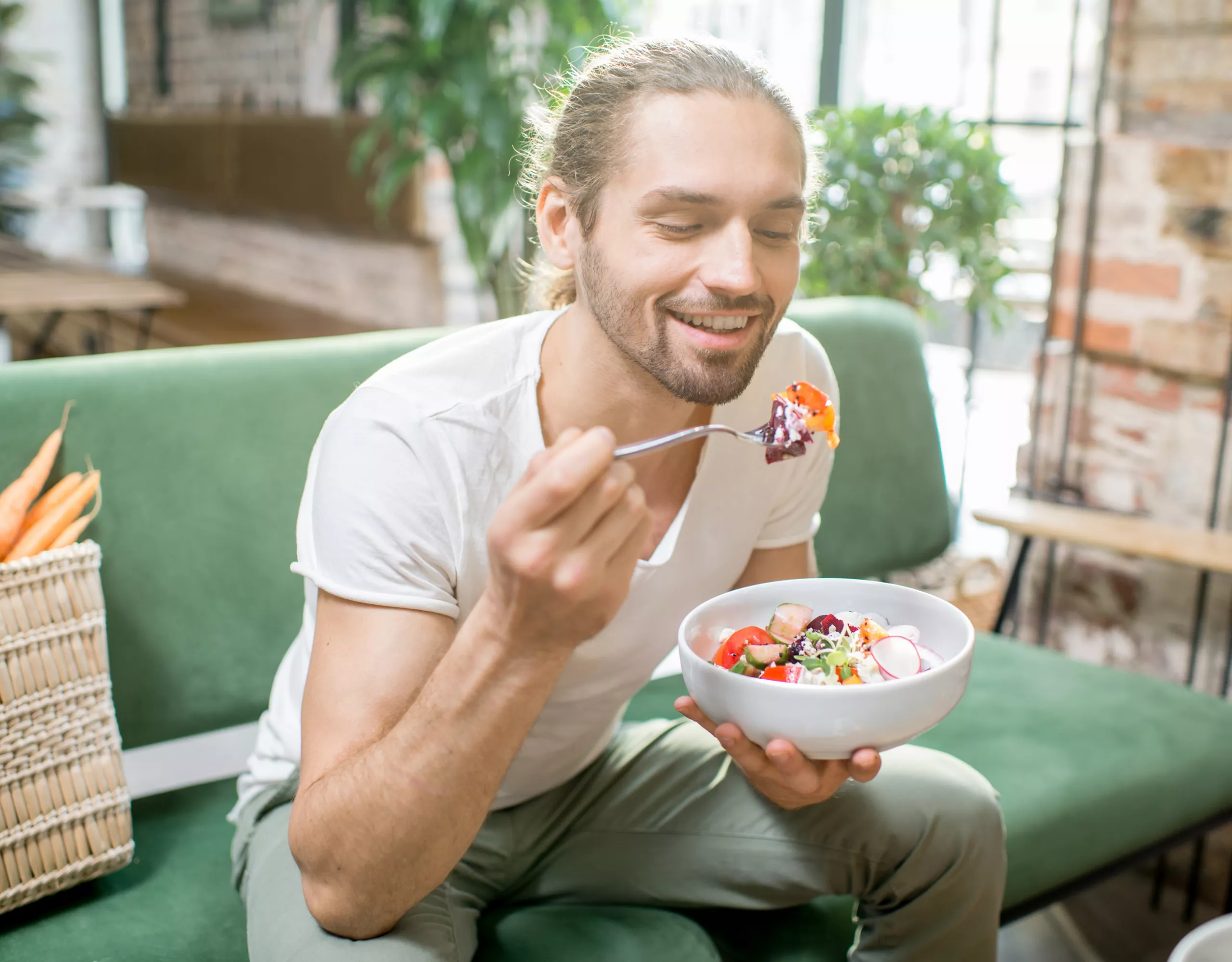 Mann isst Salat auf Couch