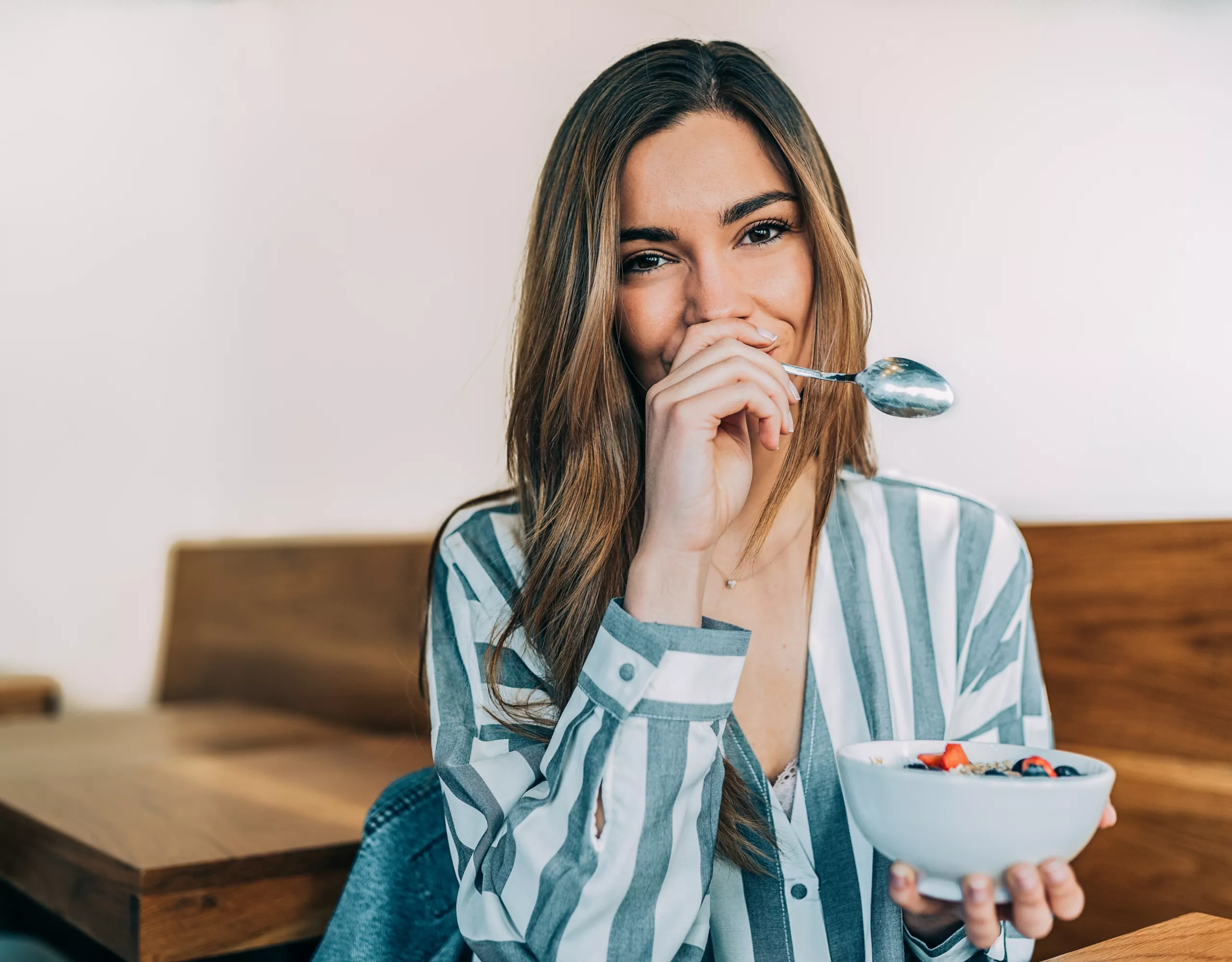 Frau isst und hält sich die Hand mit einem Löffel vor den Mund