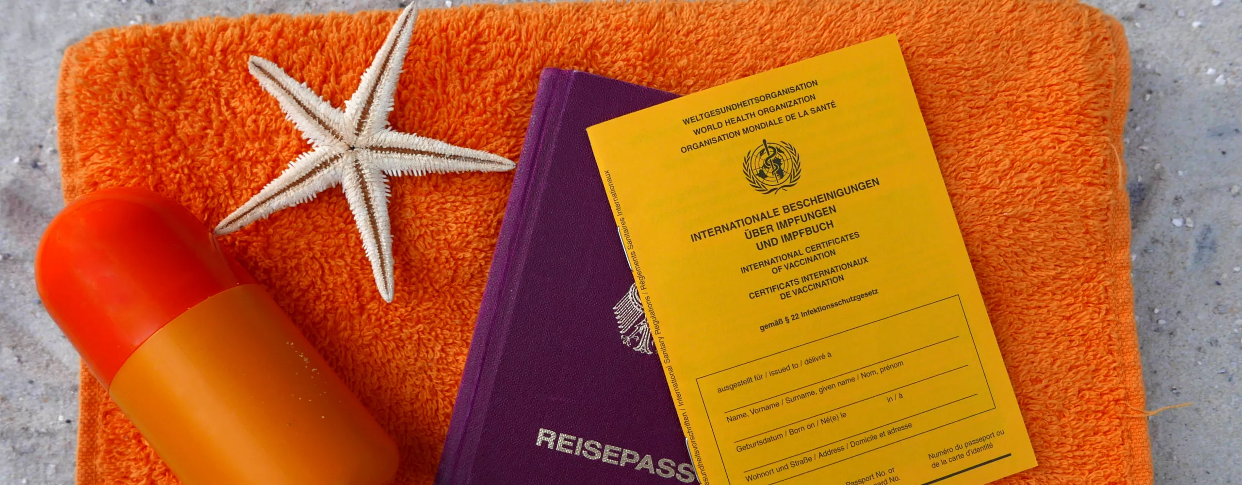 Reisepass und Impfpas liegen auf einem orangenen Handtuch