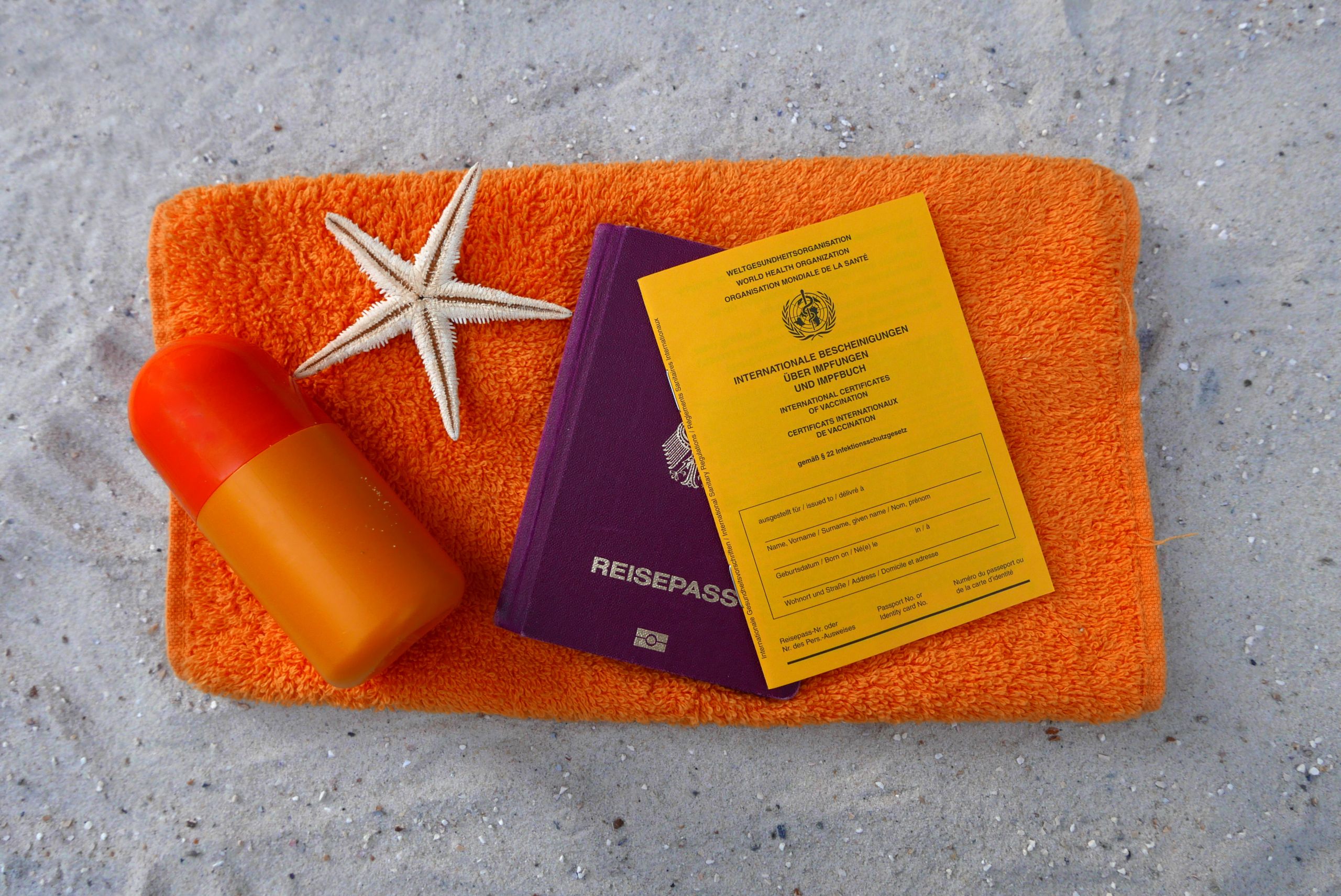 Reisepass und Impfpas liegen auf einem orangenen Handtuch