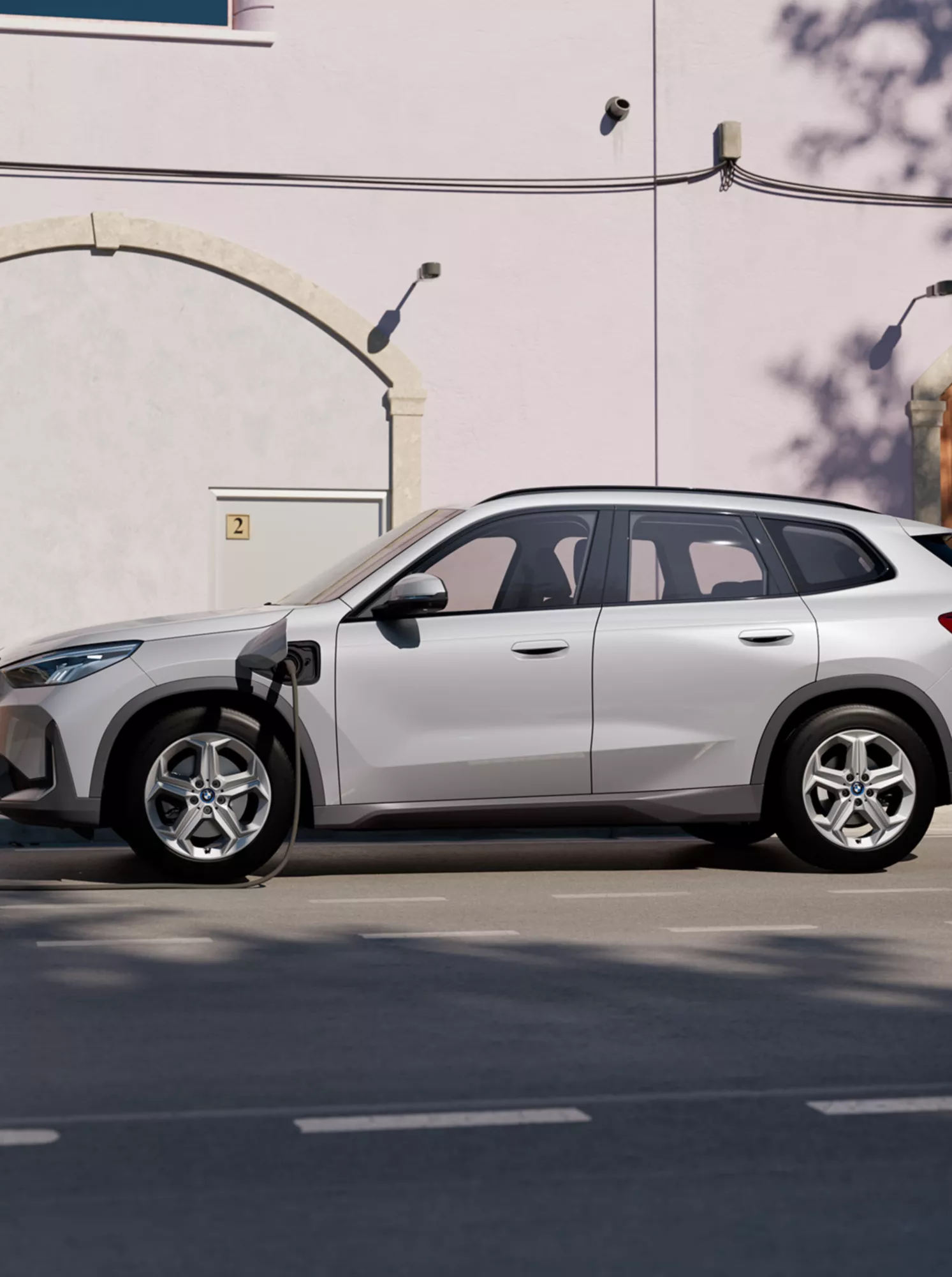 En vit BMW X1 sedd från sidan som är parkerad och laddas 