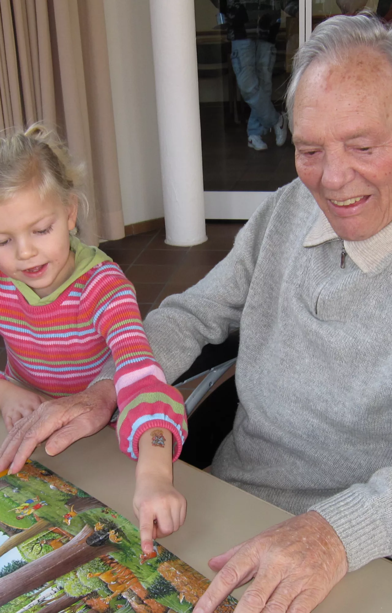 Oma sitzt mit Enkelin an einem Tisch im Seniorenheim