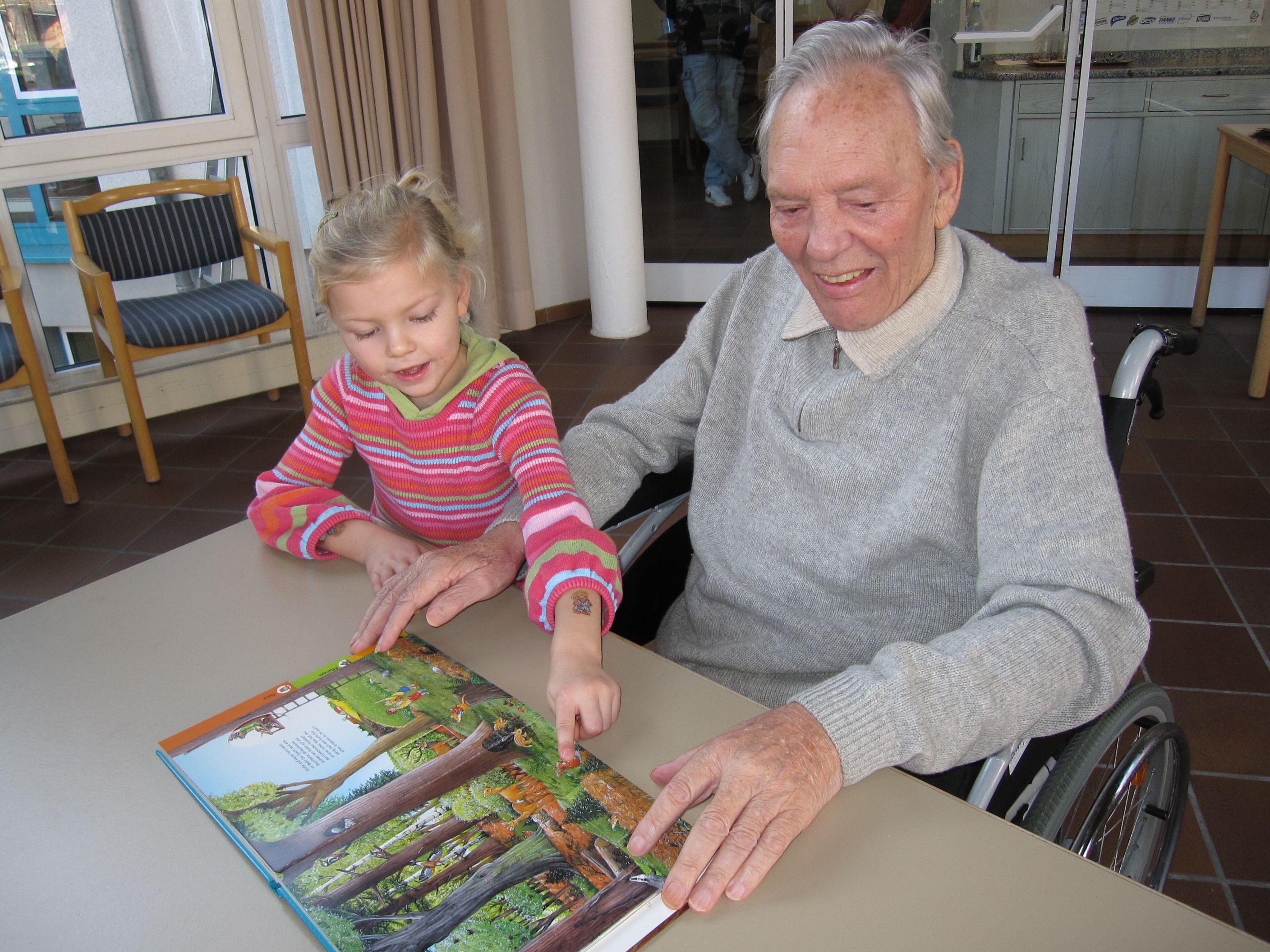 Oma sitzt mit Enkelin an einem Tisch im Seniorenheim