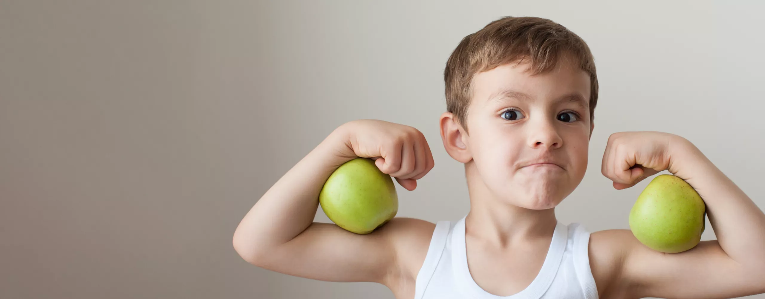 Junge zeigt seine Muskeln und hält zwei Äpfel auf den Armen 