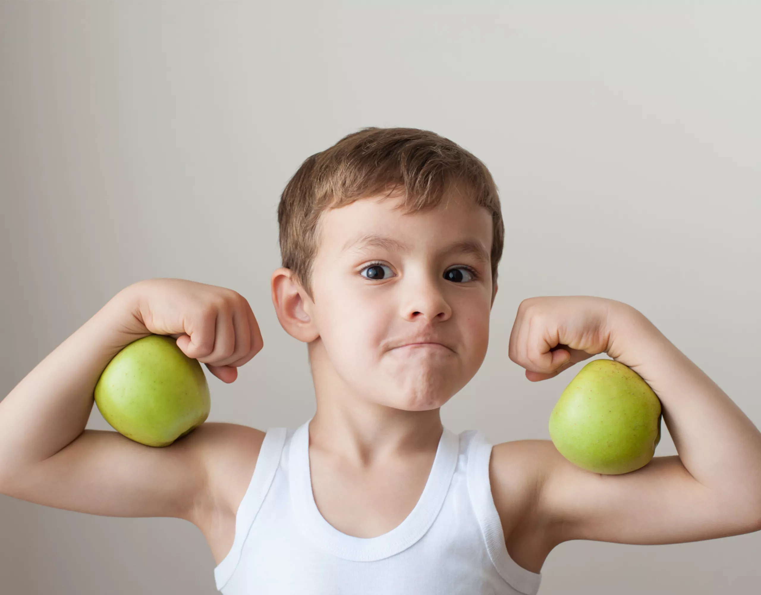 Junge zeigt seine Muskeln und hält zwei Äpfel auf den Armen 