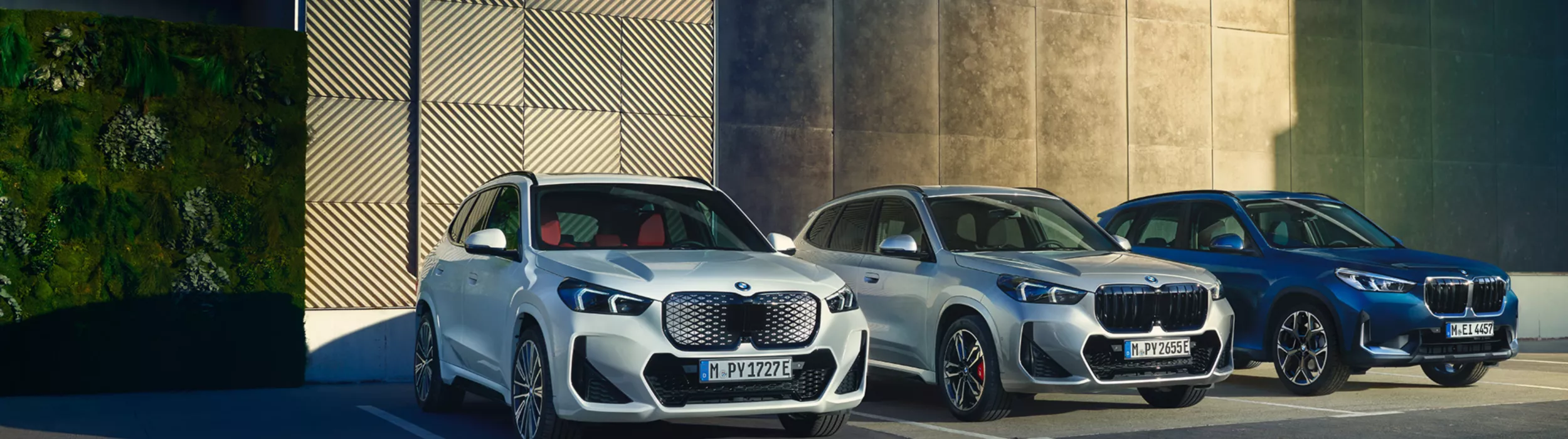 En grå BMW iX1, en grå BMW X1 och en blå BMW X1 på parkerade på parkering