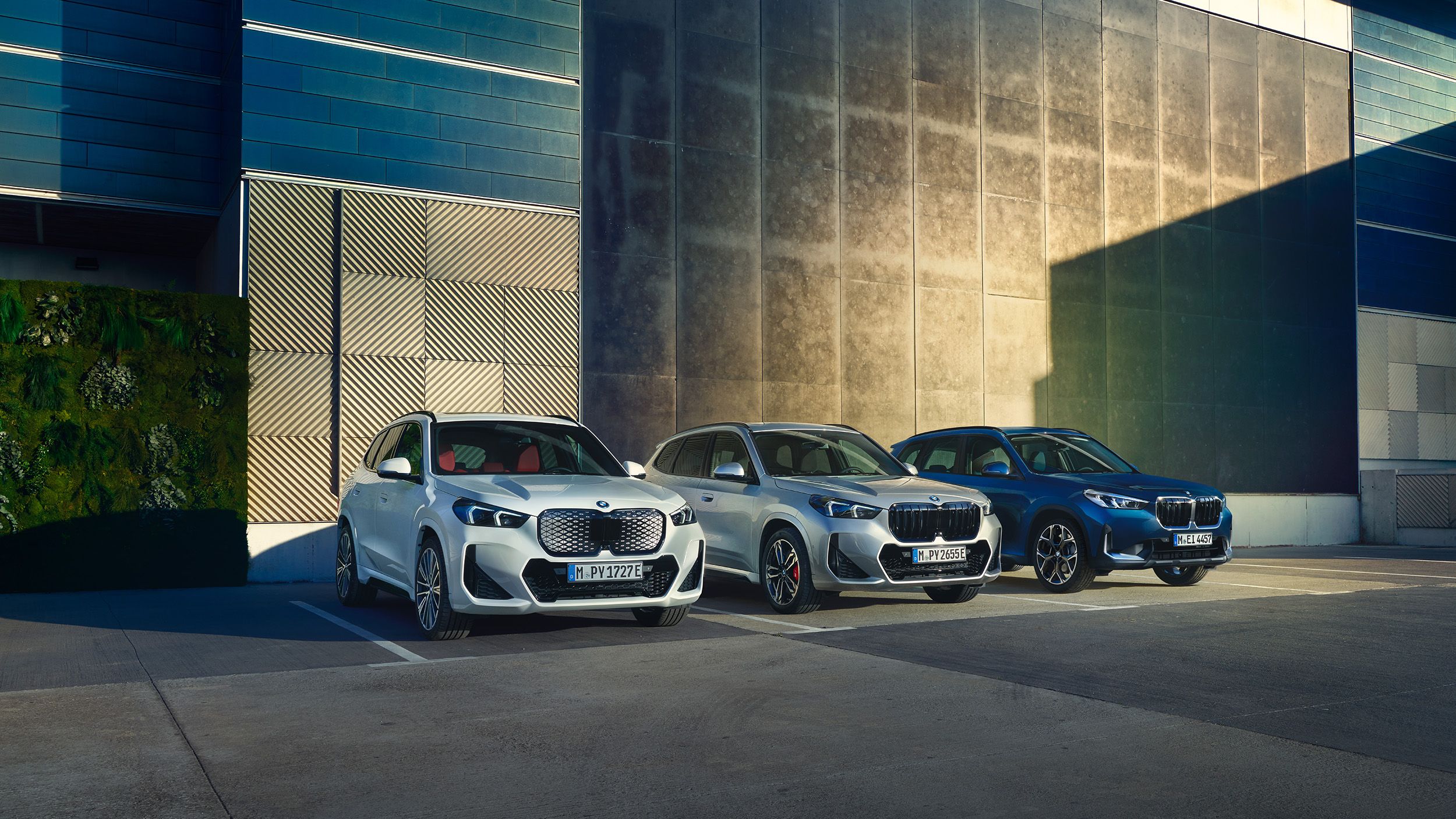 En grå BMW iX1, en grå BMW X1 och en blå BMW X1 på parkerade på parkering