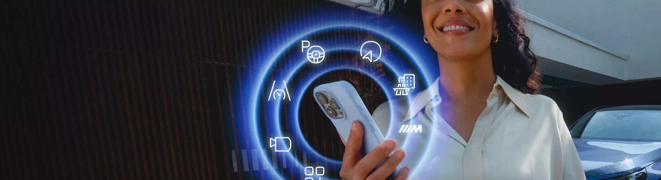 Persona che utilizza uno smartphone con le funzioni BMW ConnectedDrive visualizzate accanto a un veicolo BMW parcheggiato.