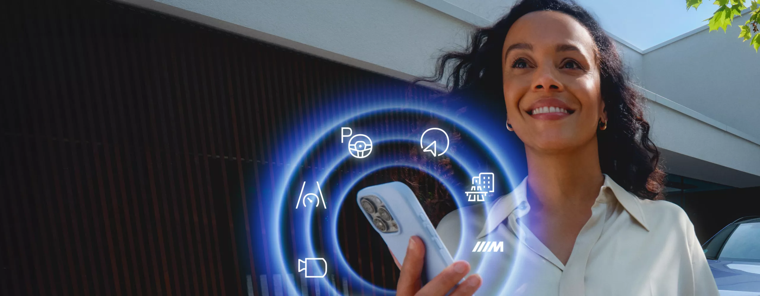 Persona utilizando un smartphone con funciones BMW ConnectedDrive mostradas junto a un vehículo BMW estacionado.