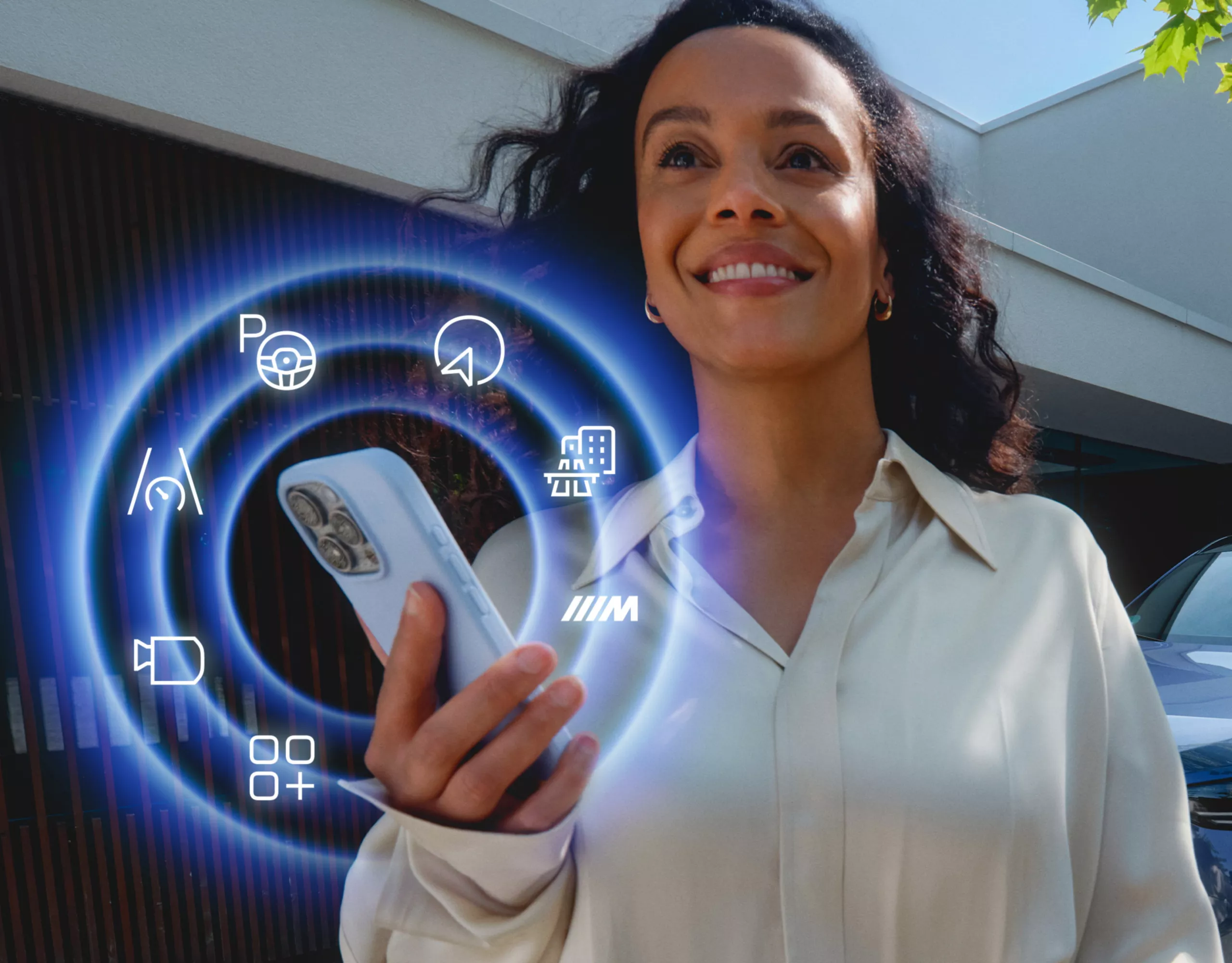 Persona che utilizza uno smartphone con le funzioni BMW ConnectedDrive visualizzate accanto a un veicolo BMW parcheggiato.