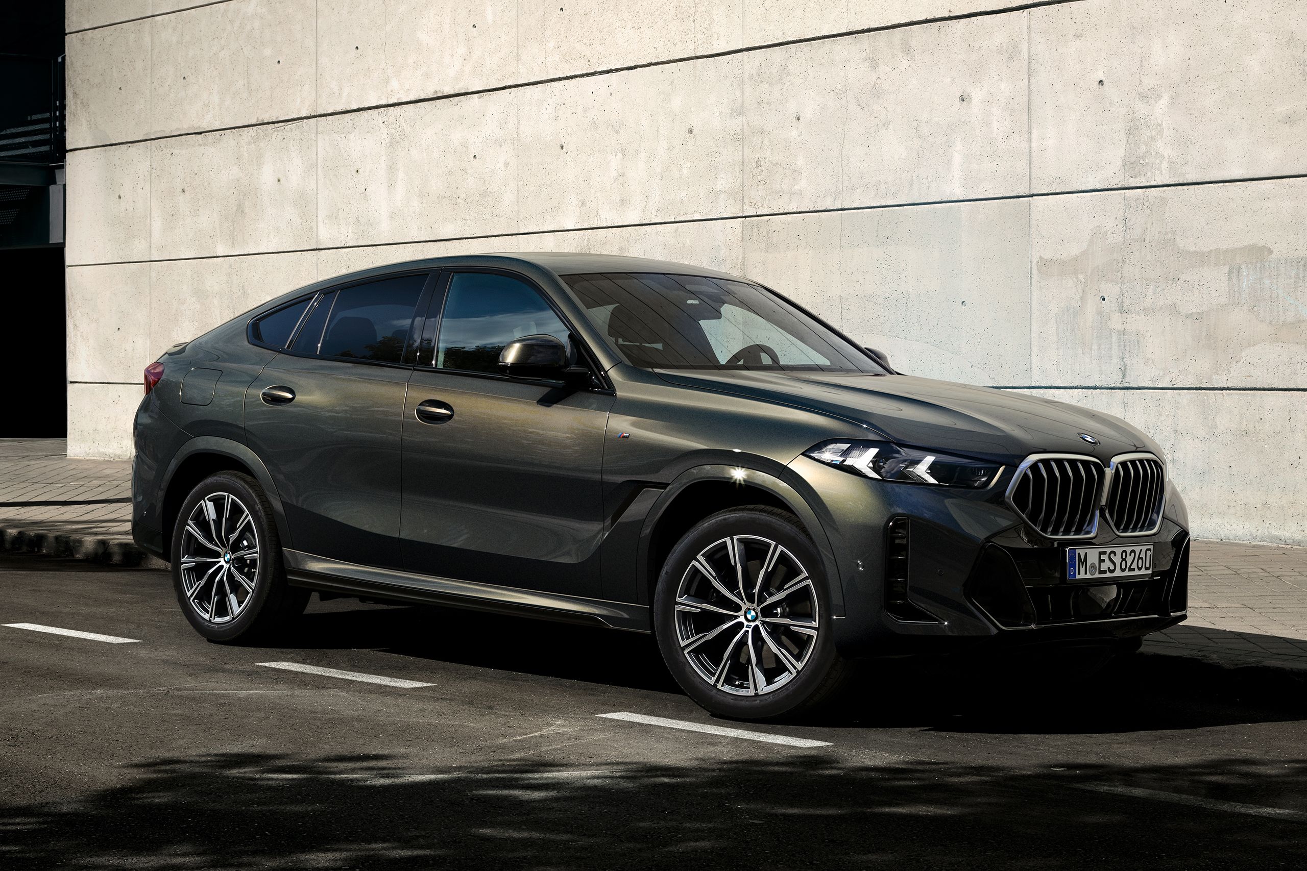 モダンな建物の前に停められたBMW X6とその横を歩く男性
