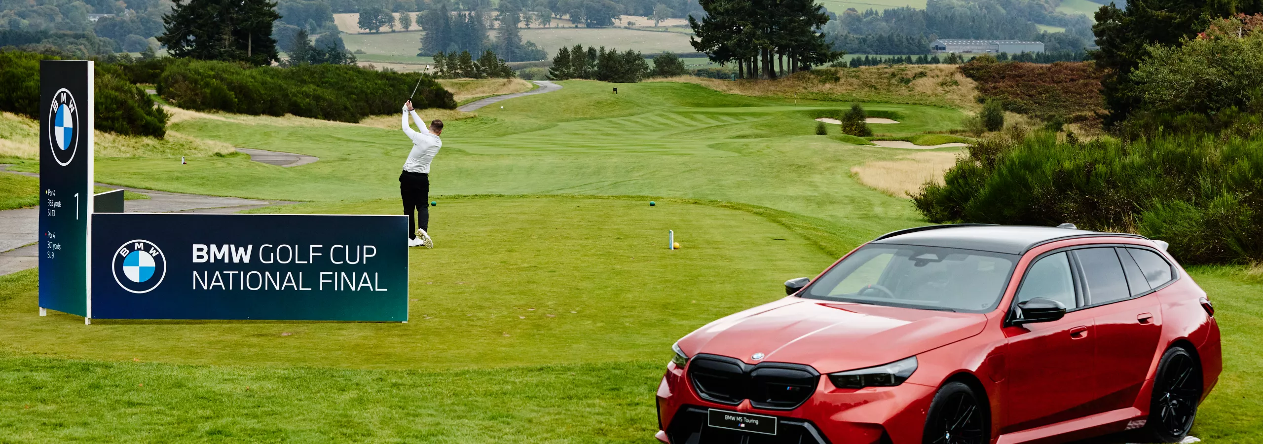 A golfer swings on a lush green course during the BMW Golf Cup National Final. A red BMW car is parked nearby, with scenic hills in the background.