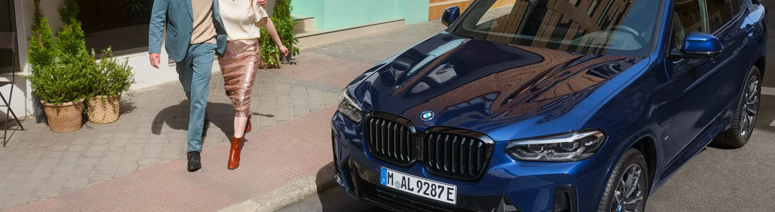 Paar hält sich in den Armen und läuft an einem BMW vorbei