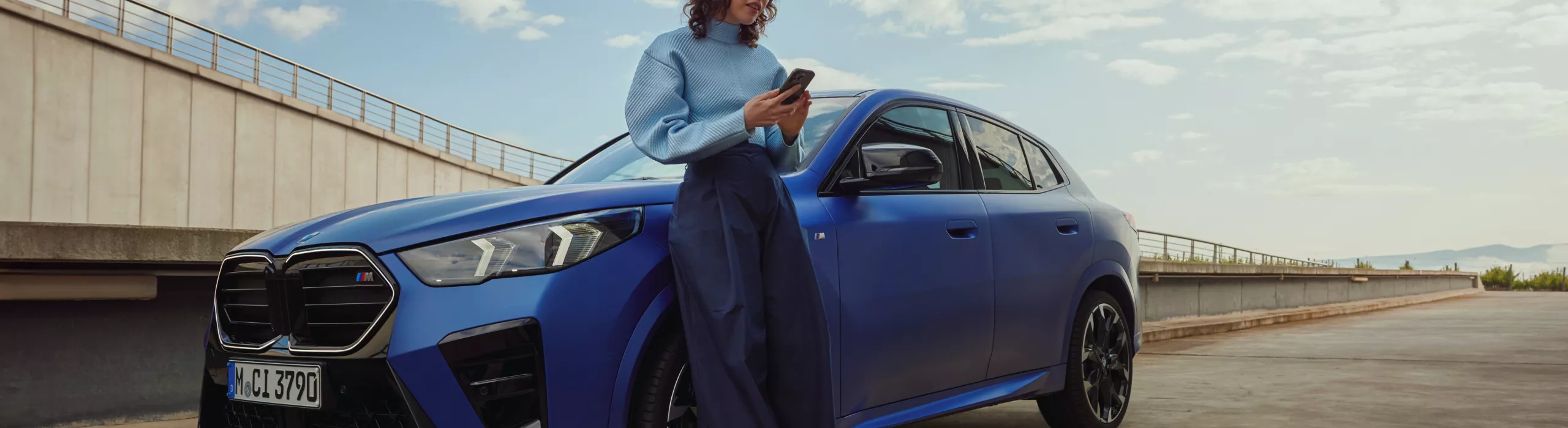 A man is approaching a BMW X2. Around the vehicle, the 3 phases of the digital key featuring the welcome light, unlocking of the doors and engine start are embedded in an overlay