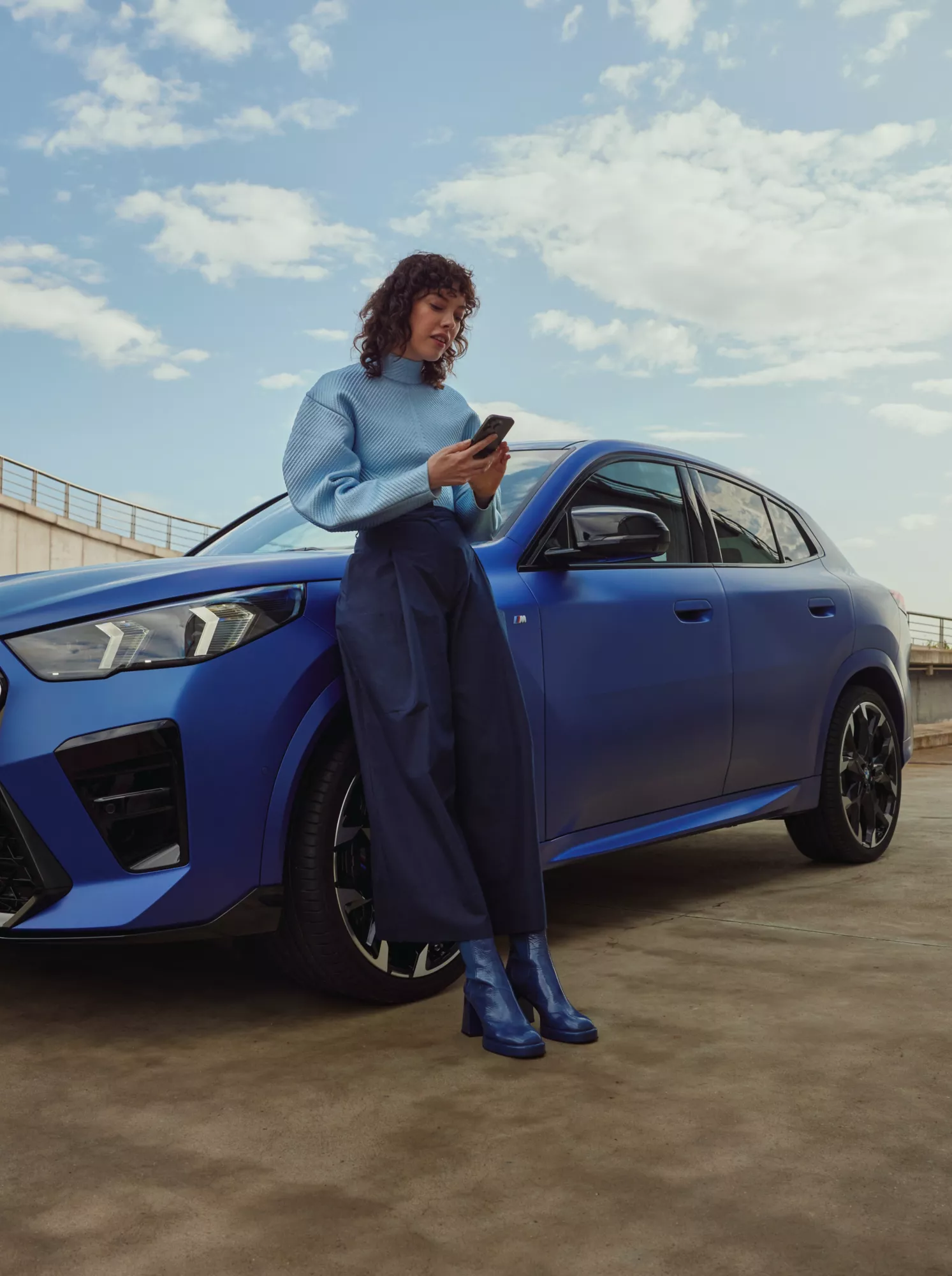 A woman stands in front of a fully electric BMW iX2