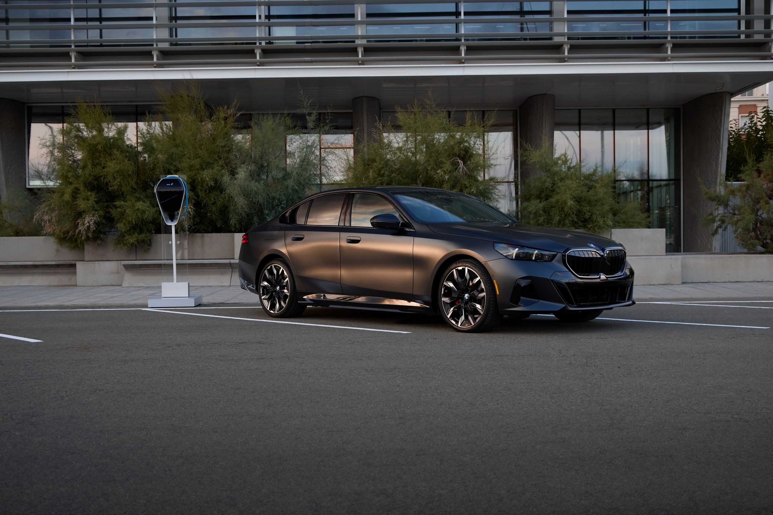The BMW 550e Sedan charges up with a BMW Wallbox Charger outside a modern building
