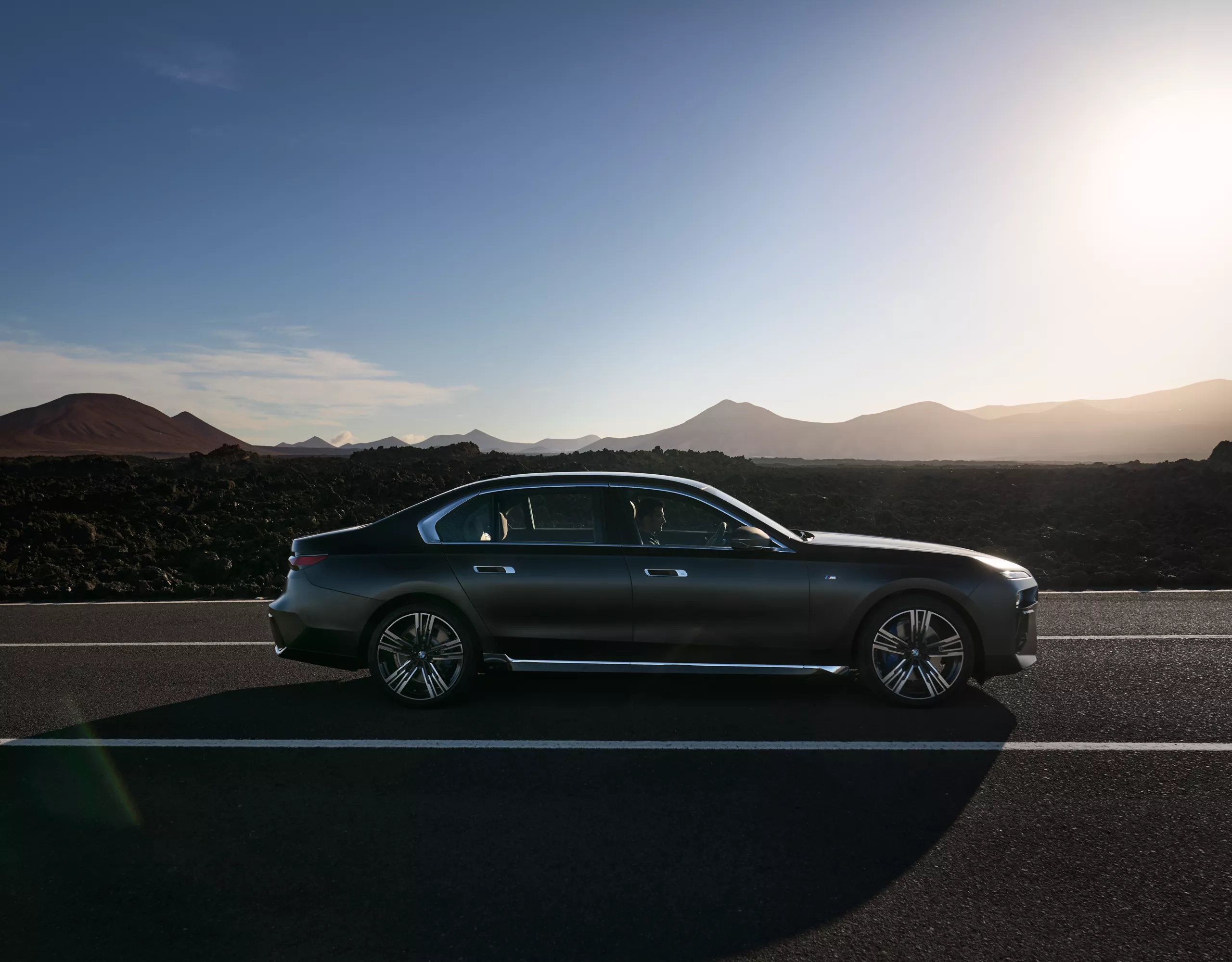 BMW 7 series sedan on a gravel road with red mountains and lakes in the background