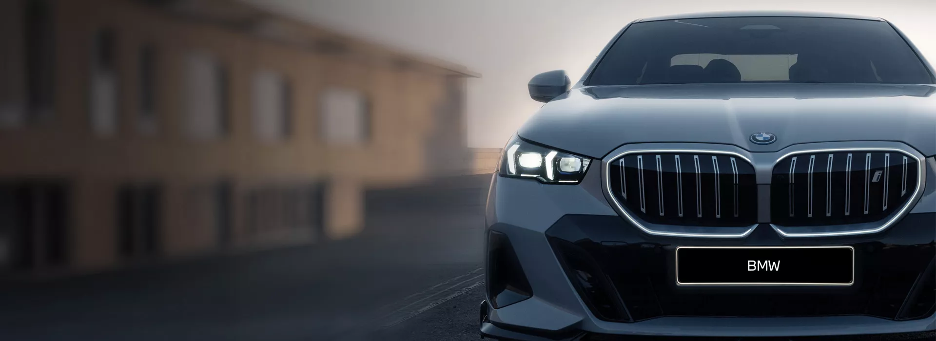 A BMW iX3 is driving on a wet, elevated road in front of a clear blue sky with few clouds