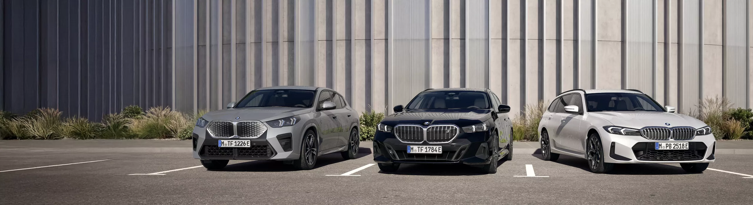 Une BMW X5 hybride rechargeable en Manhattan Metallic est stationnée devant un bâtiment moderne. Une personne se tient avec décontraction près de la porte conducteur du SUV de luxe, mettant en valeur son design haut de gamme, ses proportions sportives et l’élégance de sa peinture métallisée