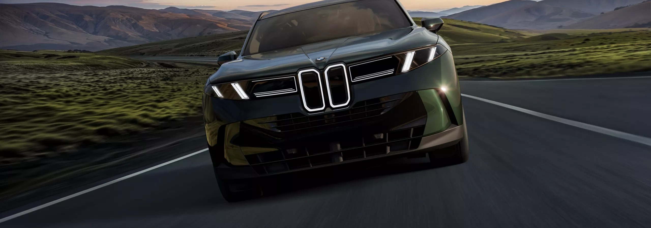 A frontal shot of the BMW X5 as it drives on a highway cutting through lush hills