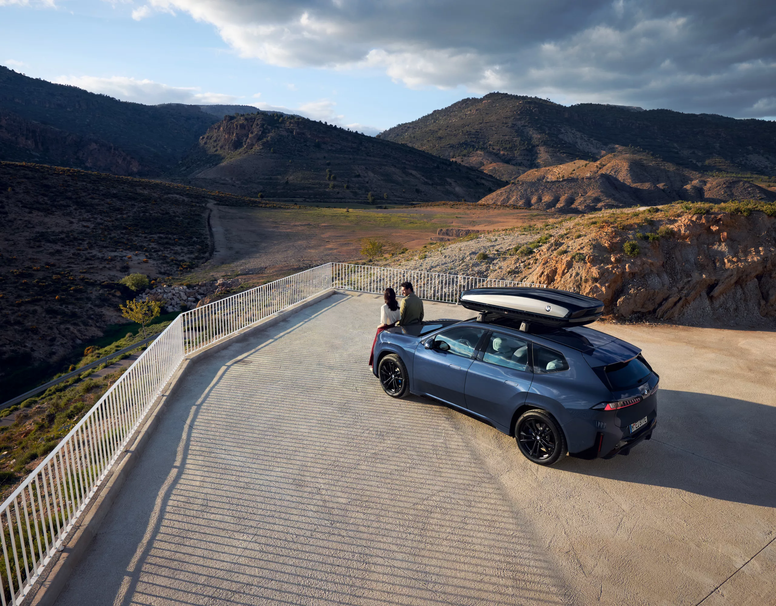 Two people standing in front of a BMW iX3 with rooftop box gazing into the distance