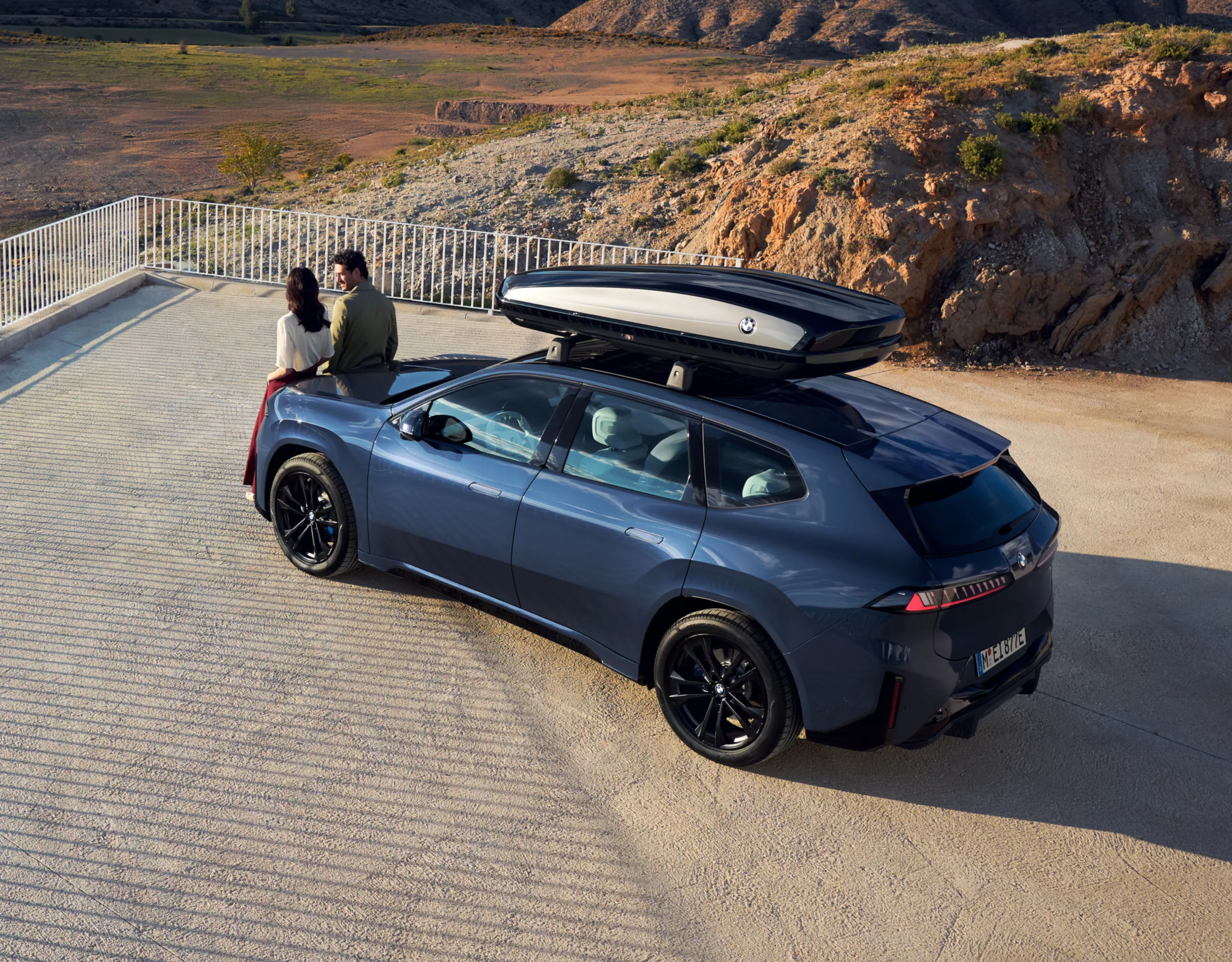 Zwei Personen stehen vor einem BMW iX3 mit Dachbox und blicken in die Ferne