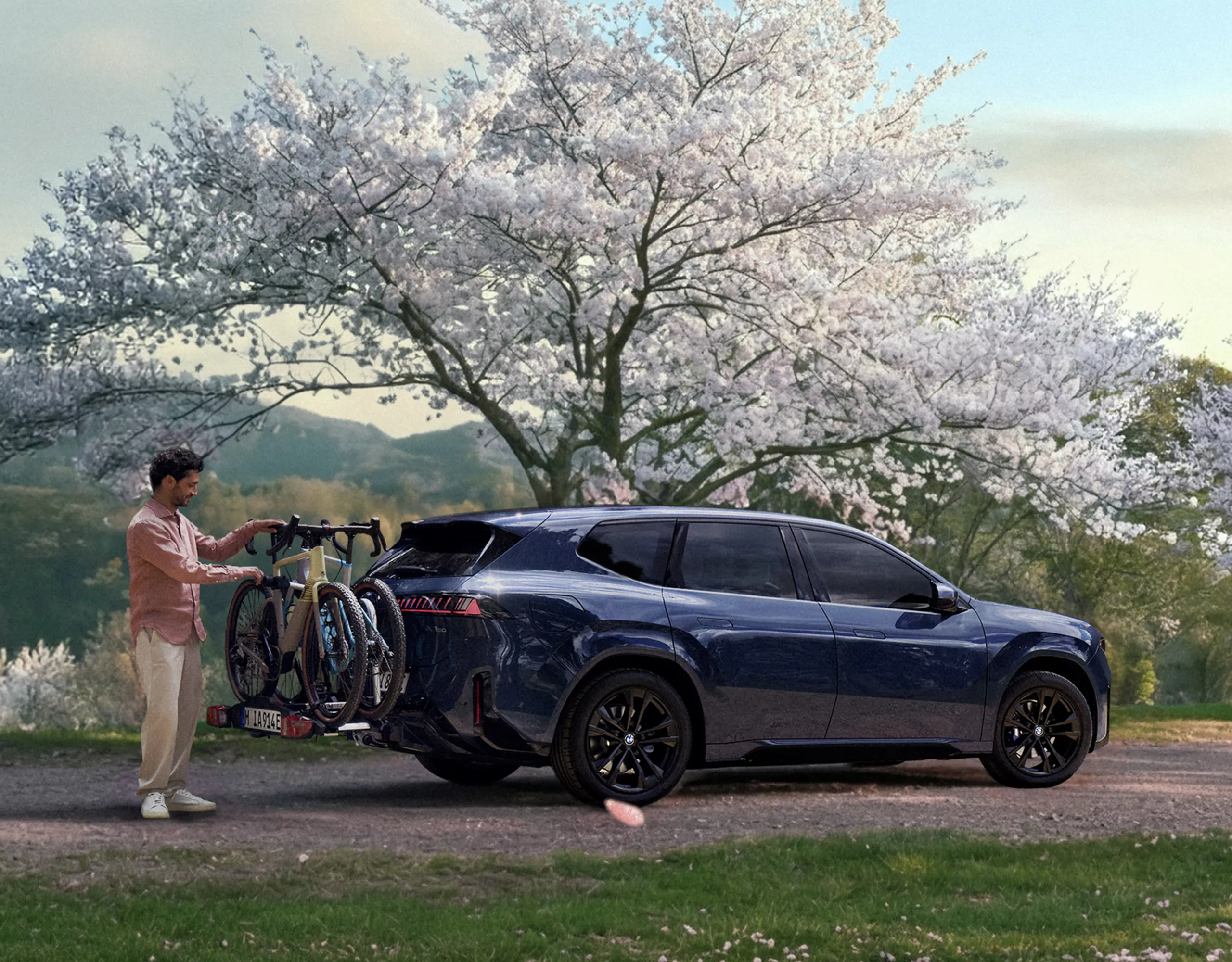 BMW mit Fahrradträger am Heck in einer Frühlingslandschaft, während eine Person die Fahrräder vorbereitet