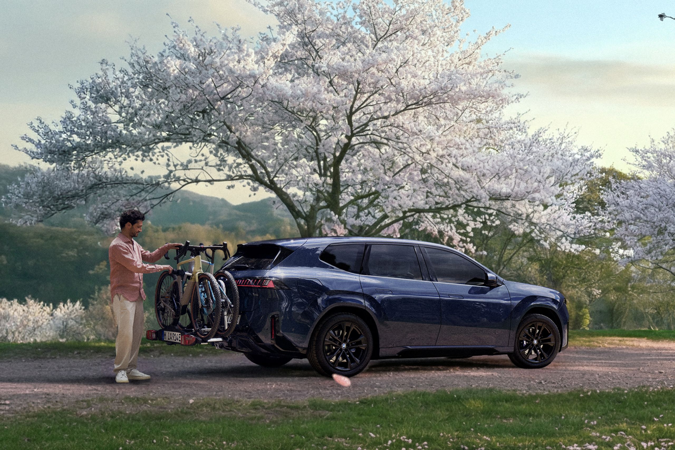 BMW mit Fahrradträger am Heck in einer Frühlingslandschaft, während eine Person die Fahrräder vorbereitet