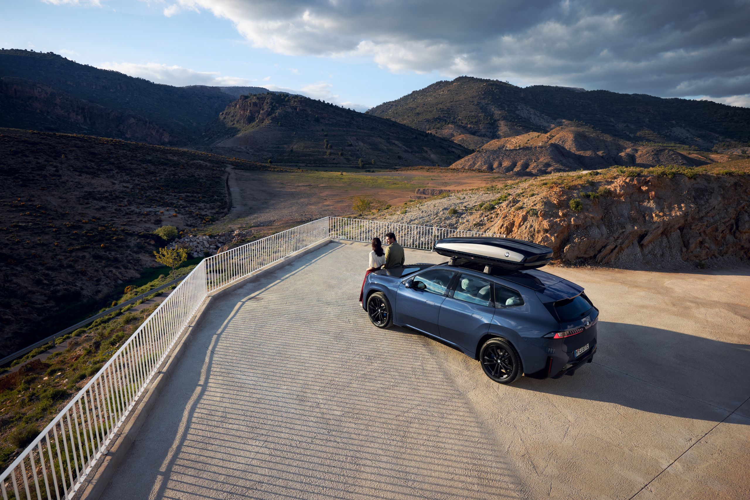 Two people standing in front of a BMW iX3 with rooftop box gazing into the distance 