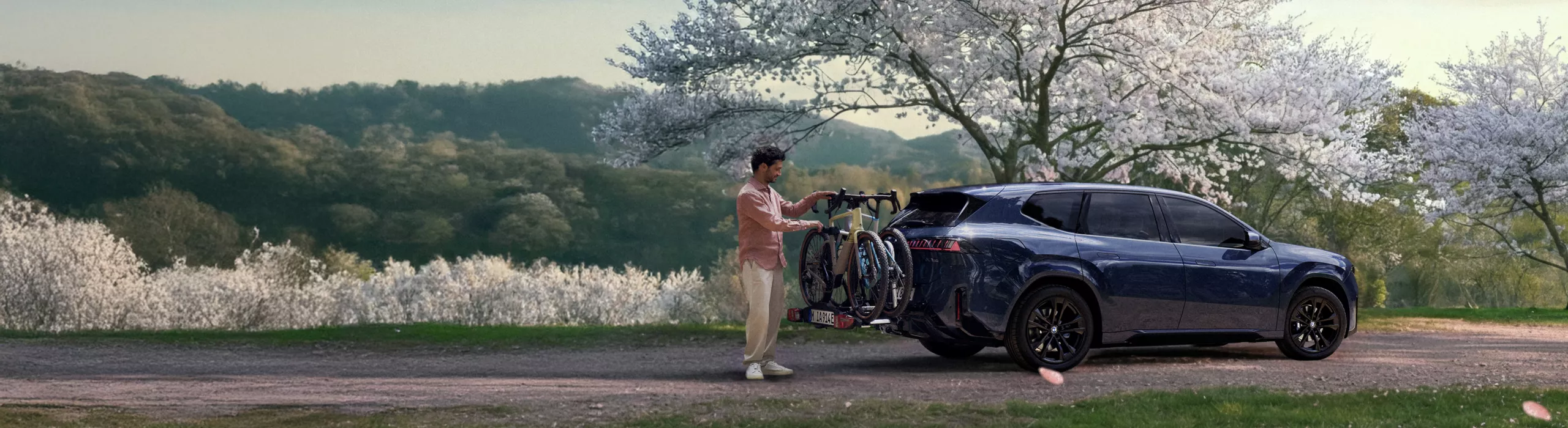 BMW mit Fahrradträger am Heck in einer Frühlingslandschaft, während eine Person die Fahrräder vorbereitet