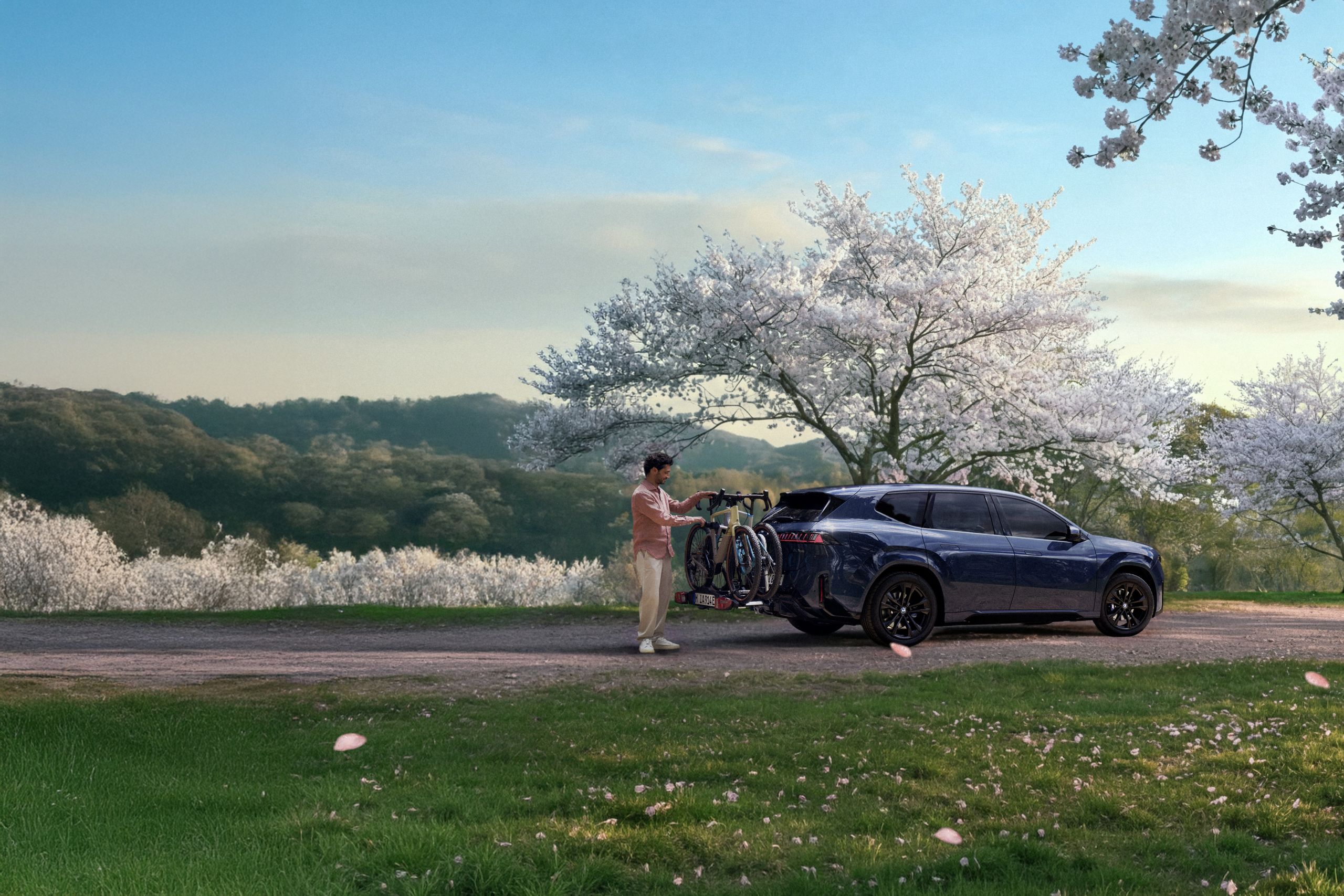 BMW mit Fahrradträger am Heck in einer Frühlingslandschaft, während eine Person die Fahrräder vorbereitet