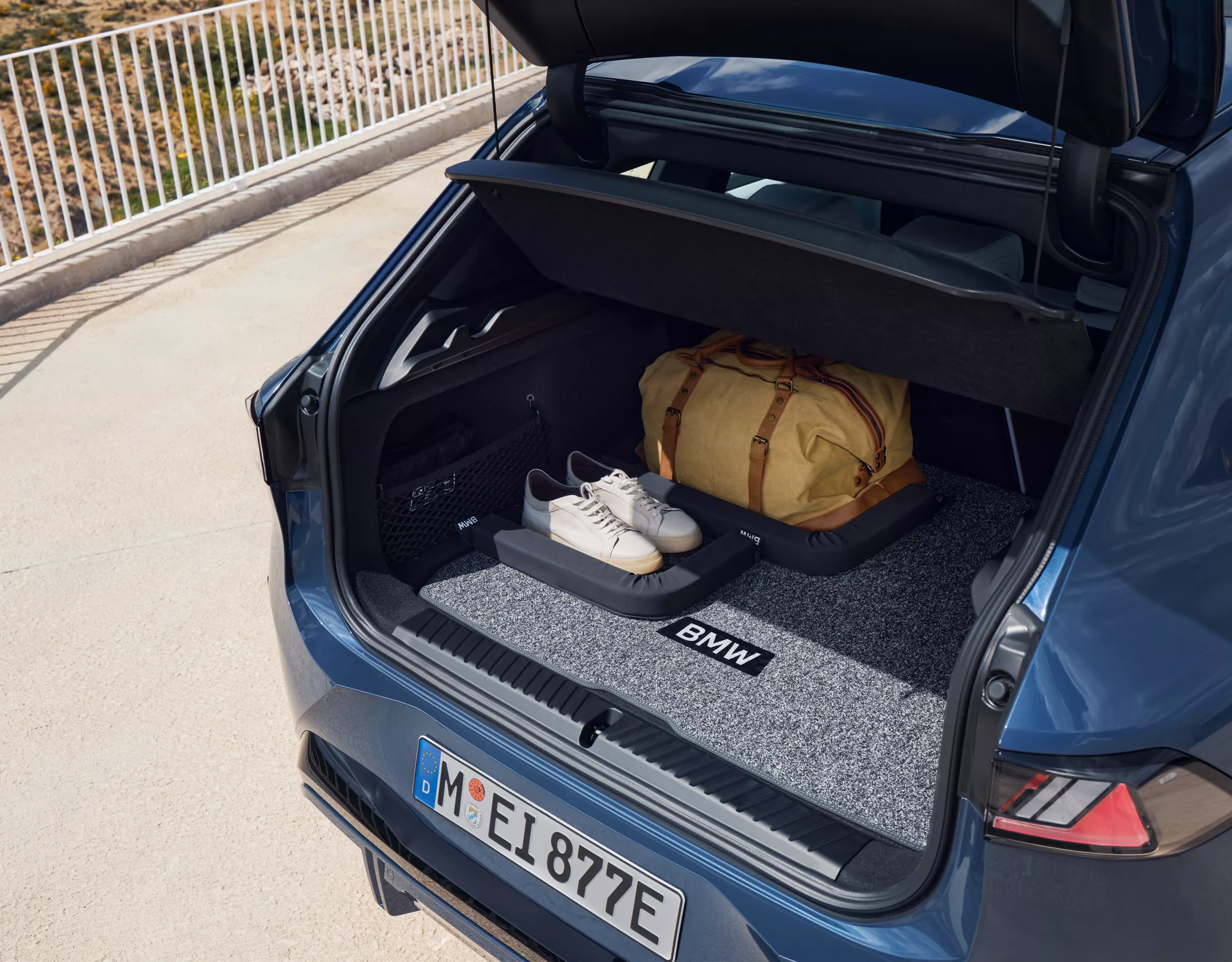 Coffre ouvert dans lequel un sac de sport et des chaussures de sport sont placés sur un tapis de coffre BMW d'origine