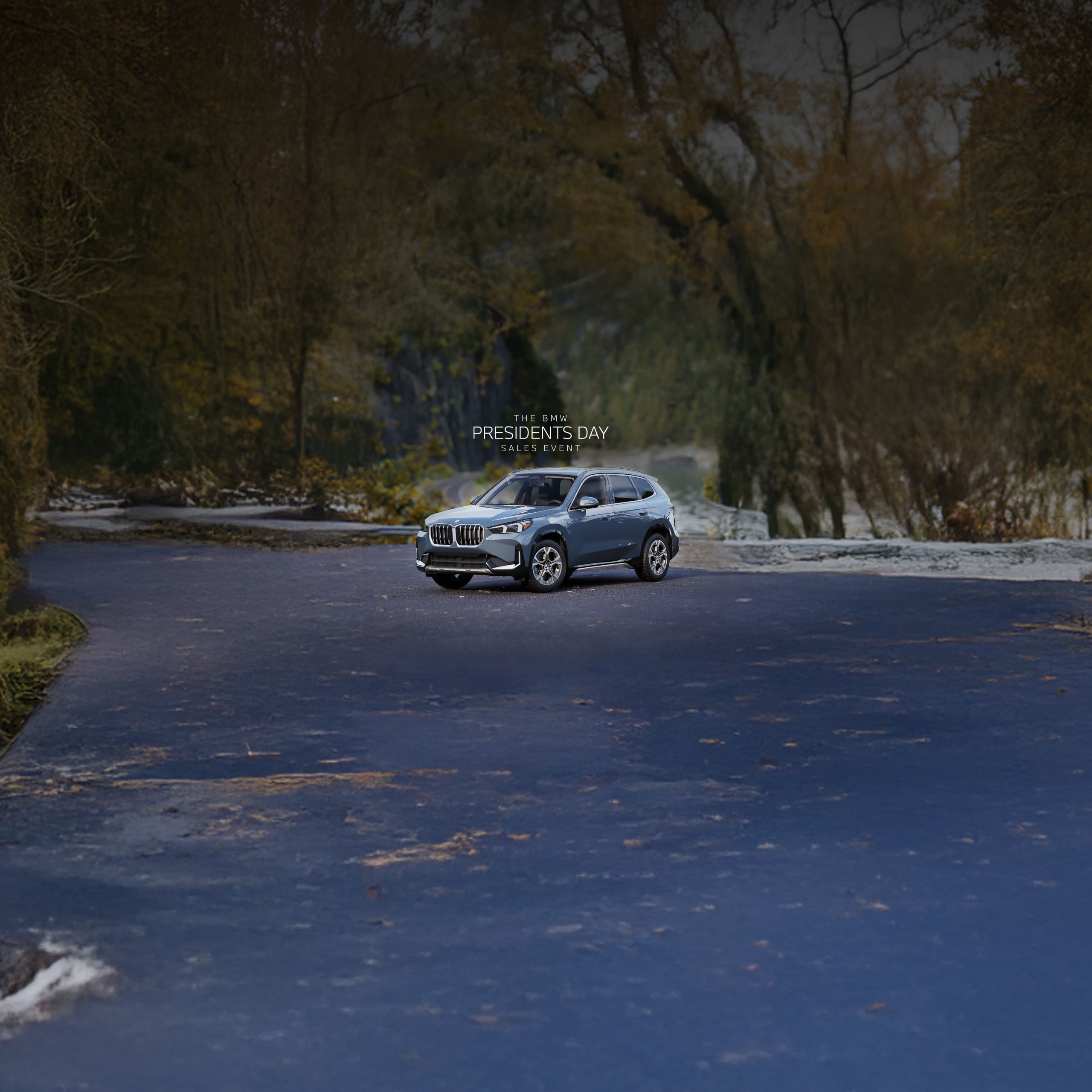 A BMW X1 sits parked on a road with cliffs and a river in the background
