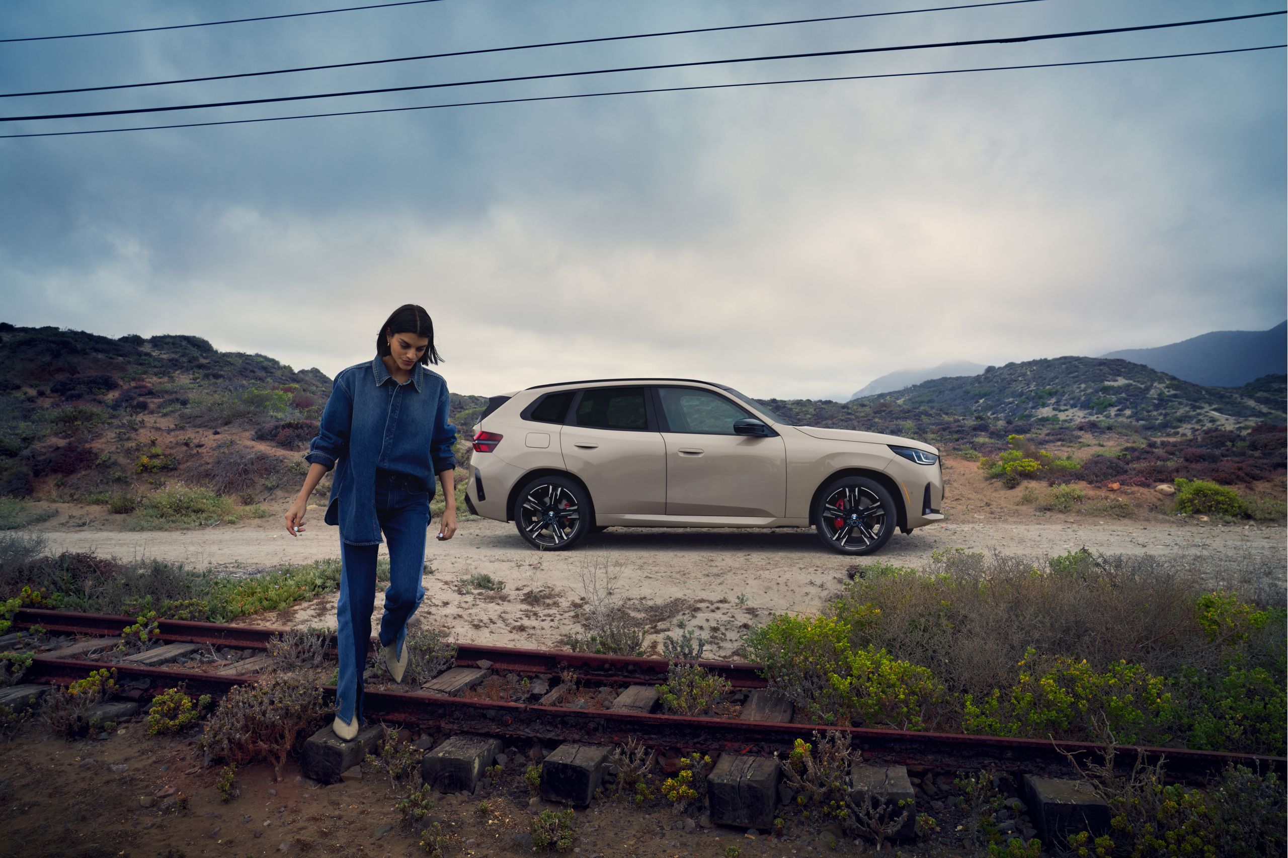 A casually dressed woman walks away from her parked BMW across an old railroad track.