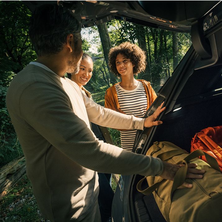 Image of family in a wooded outdoors setting, packing their bags into the trunk of a BMW