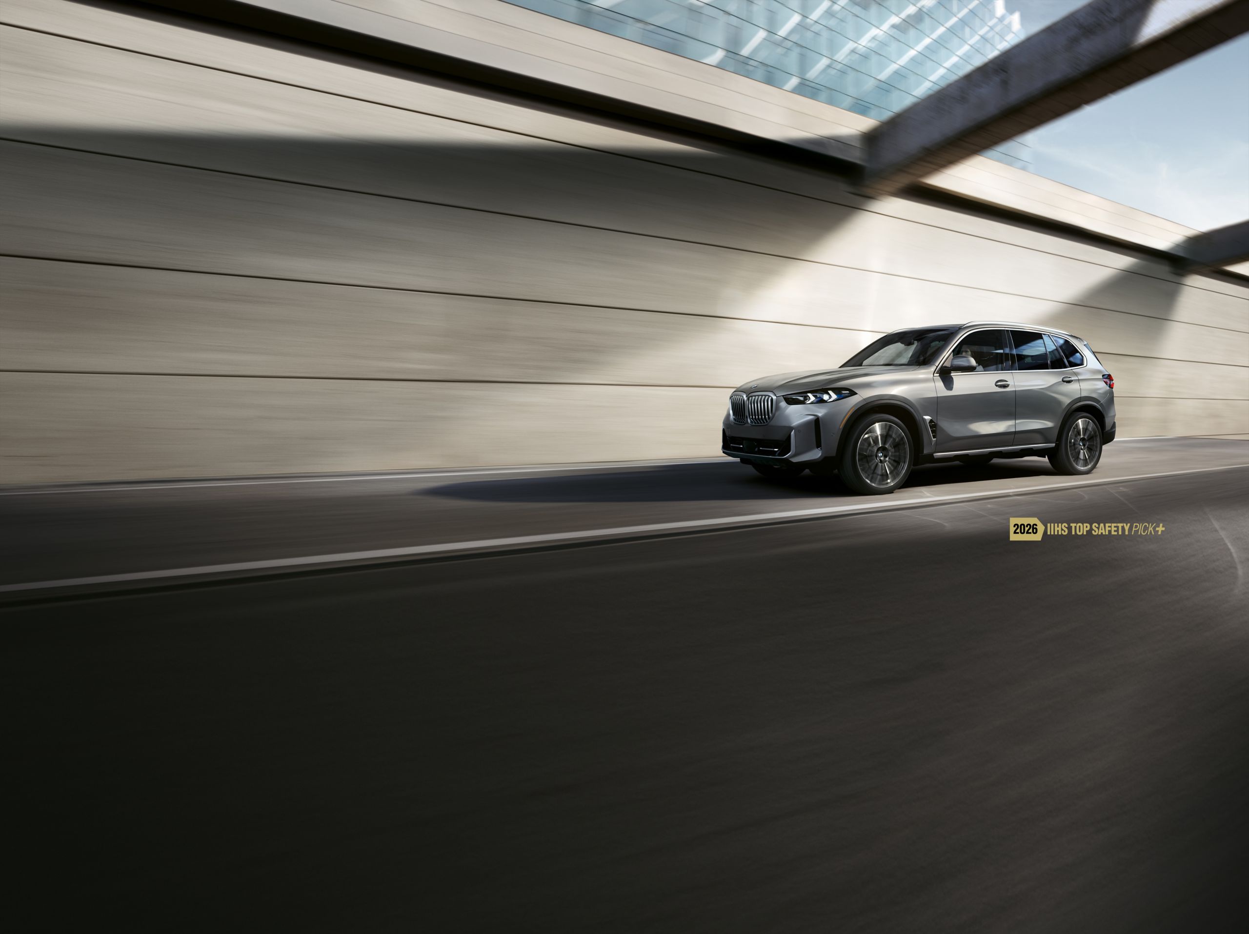 The 2026 BMW X5 xDrive40i SUV drives down an urban road beside a building