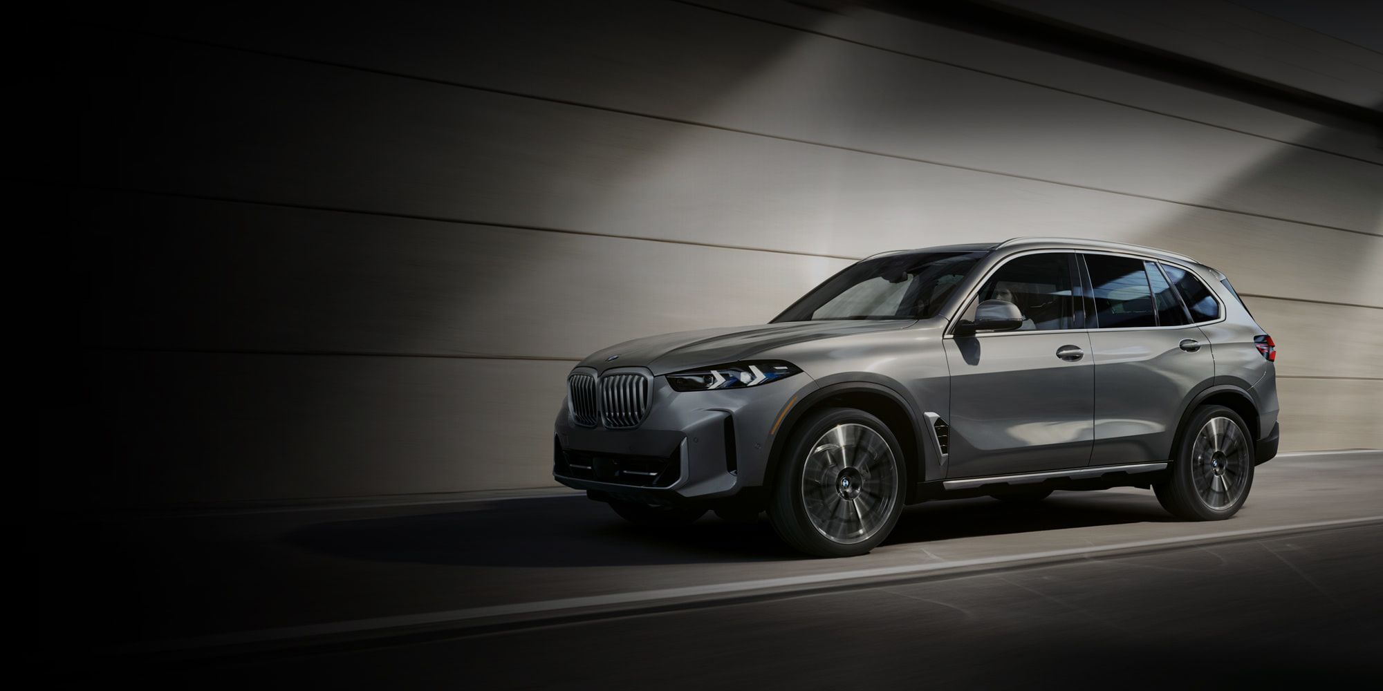 The 2026 BMW X5 xDrive40i SUV drives down an urban road beside a building