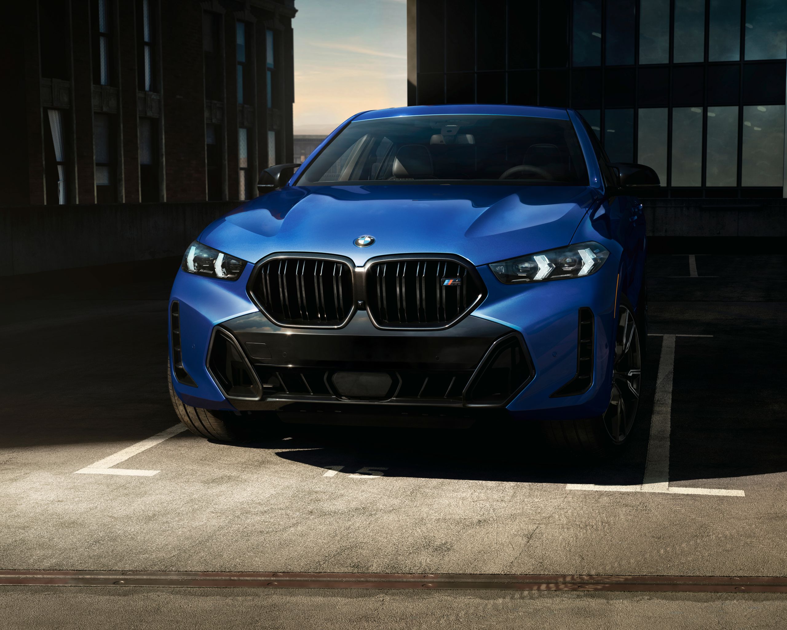 A BMW X6 M60i SUV is parked in front of a hangar door