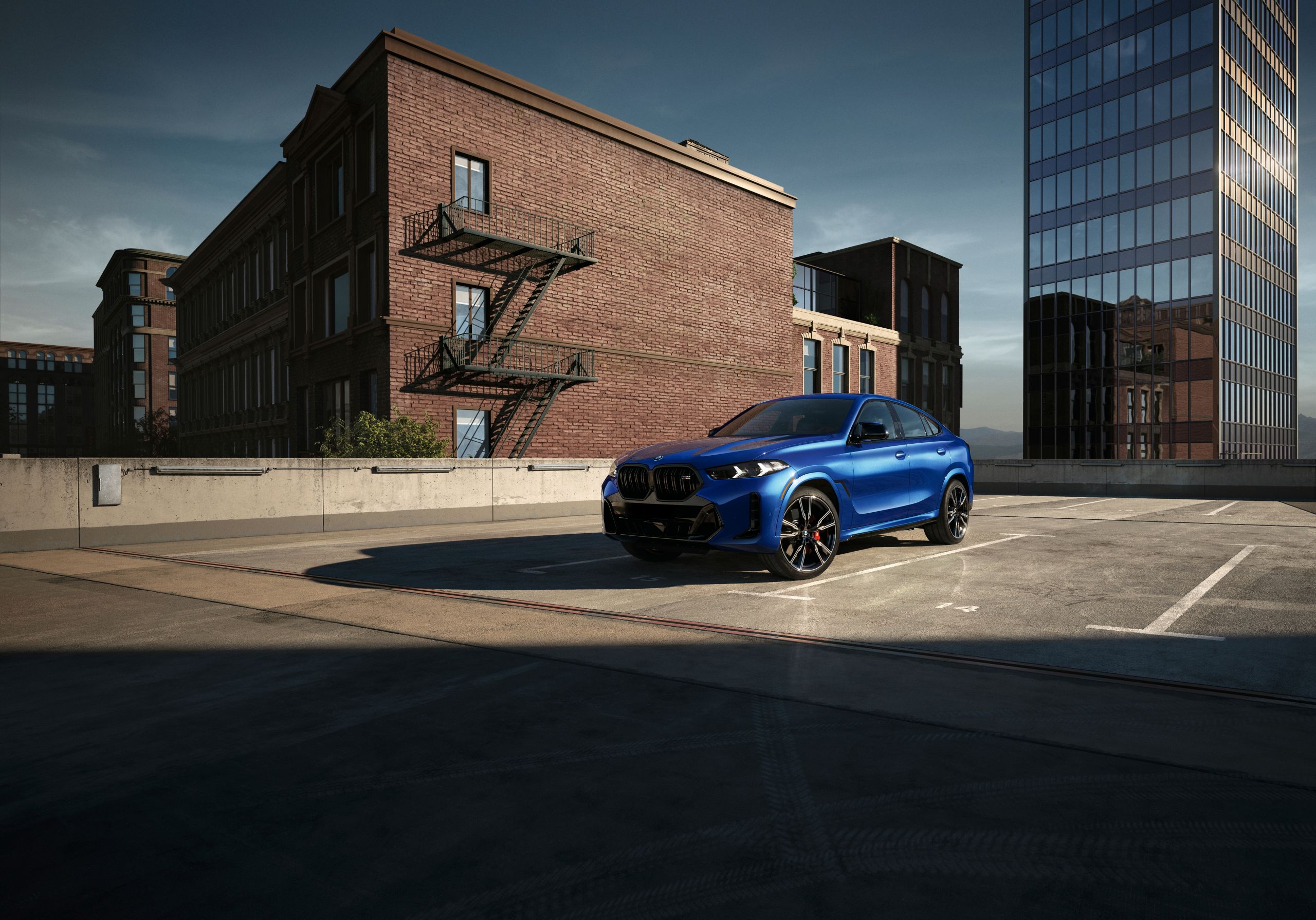 A BMW X6 M60i SUV is parked in the sunlight in front of a brick building