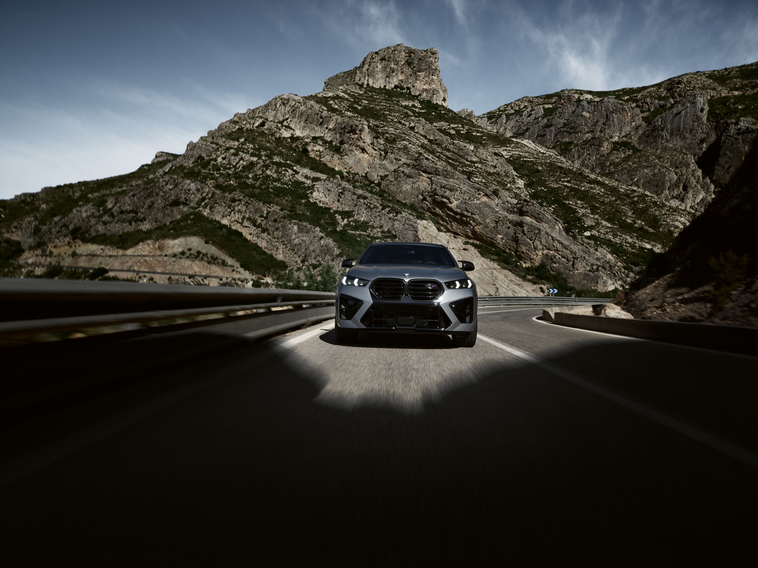 BMW X6 M Competition driving along a winding road through a valley